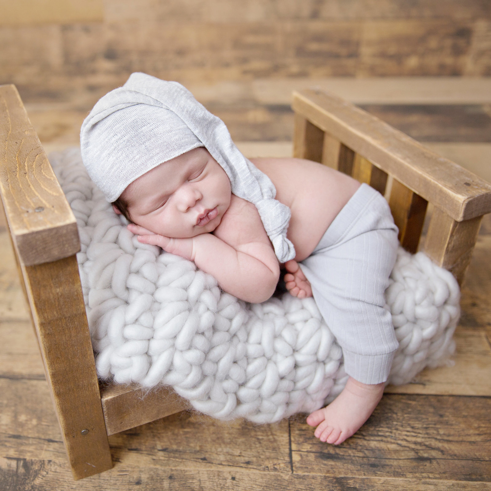 sleeping newborn baby with light grey sleepy cap on small wooden bed