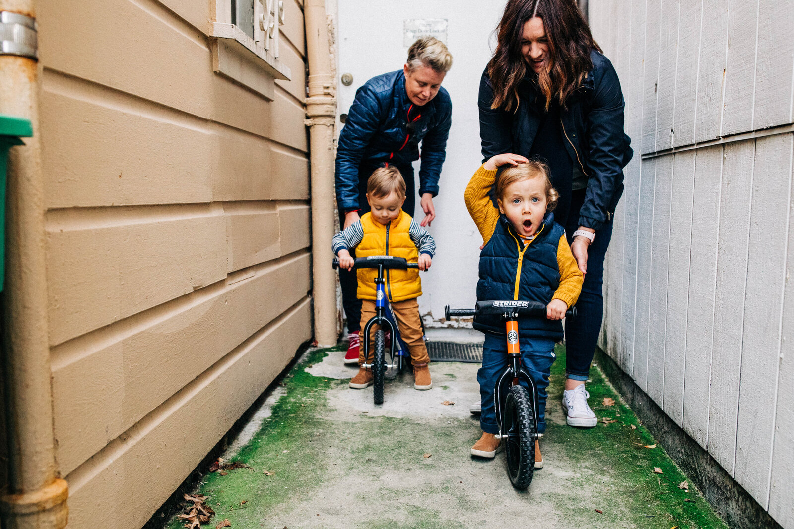 lgbtqi+ family of four in alleyway with toddler sons on bikes