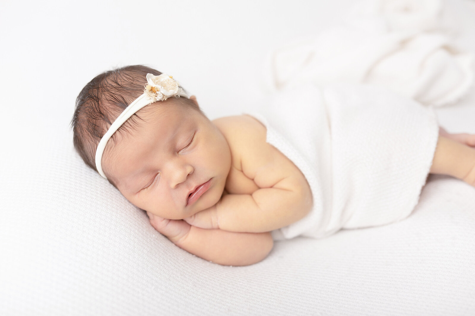 newborn baby girl in all white on a posing table
