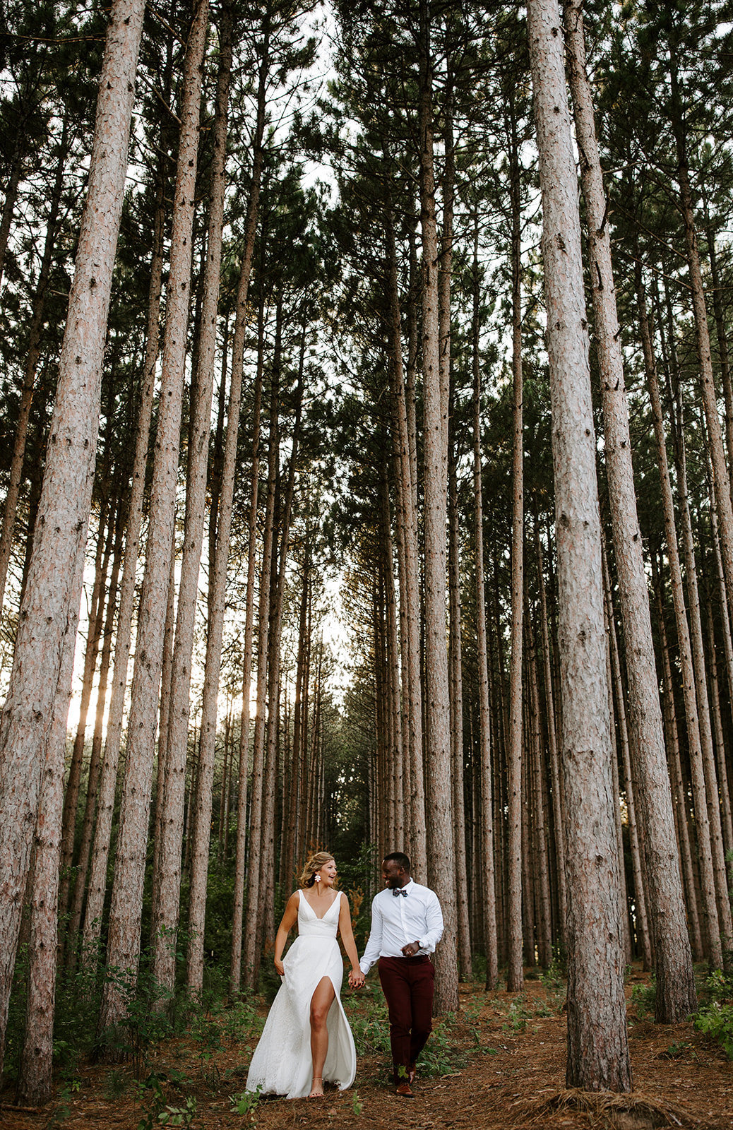Couple walking through tall pine trees holding hands during the Pinewood Wedding in Minnesota