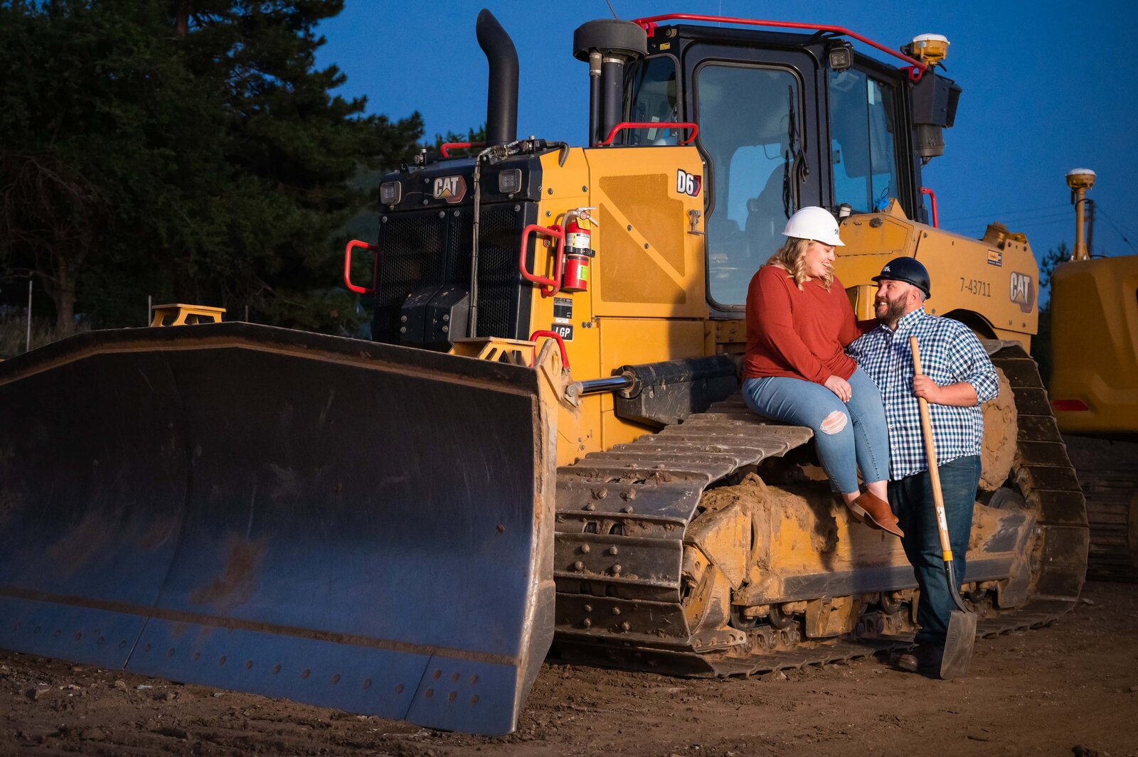 Couple with large front loader construction vehicle during engagement session.