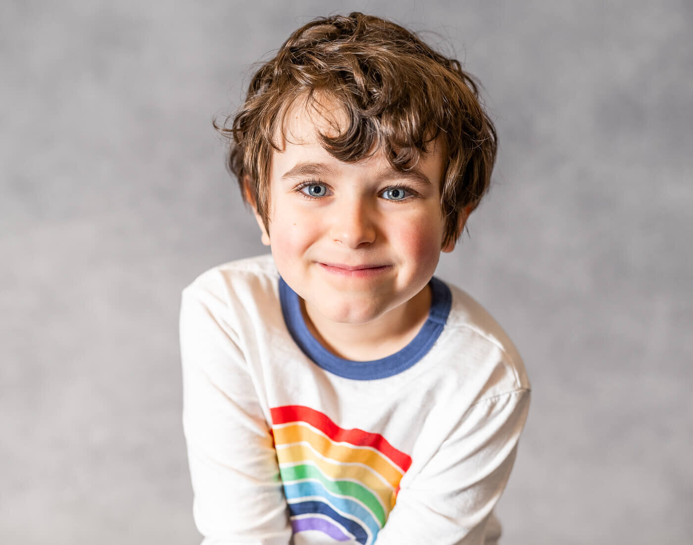 A young child smiles, their shirt with a rainbow.