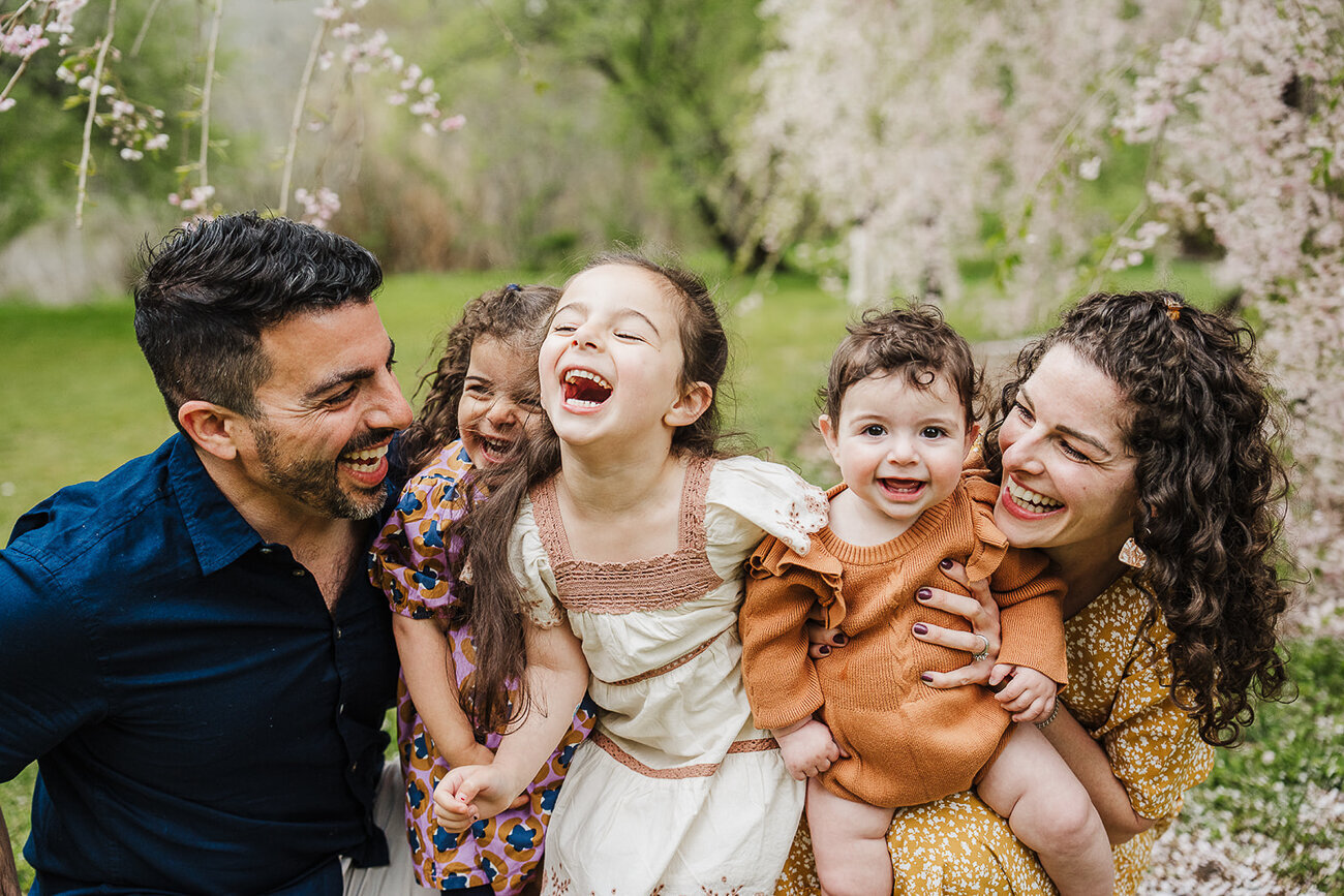 family of five laugh together with pink cherry blossoms in boston