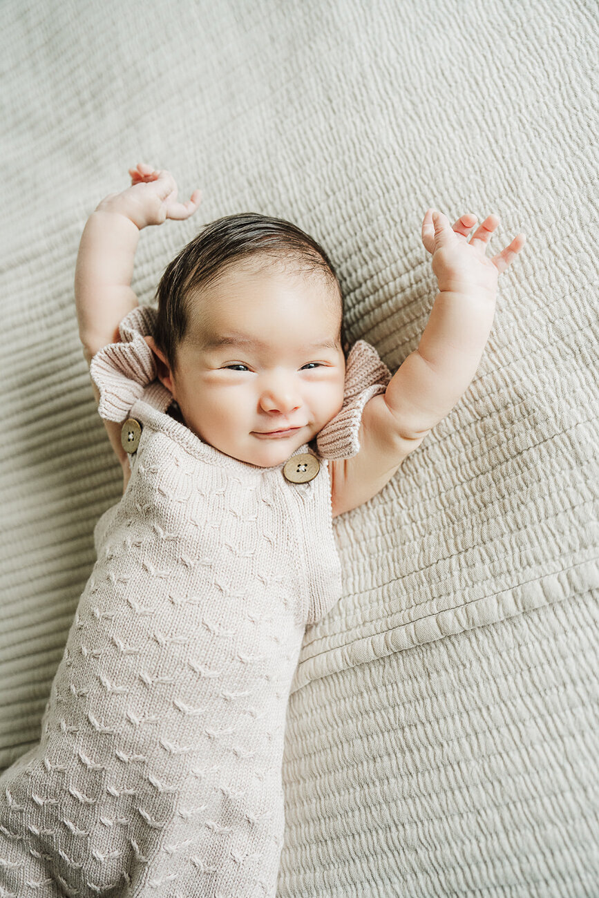 newborn stretches arms above head on bed