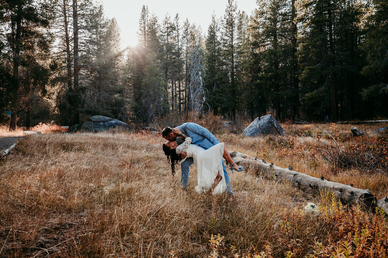 A couple shares a romantic dip in a golden meadow near Lake Tahoe, surrounded by tall pines and autumn hues, as the late afternoon sun filters through the trees.