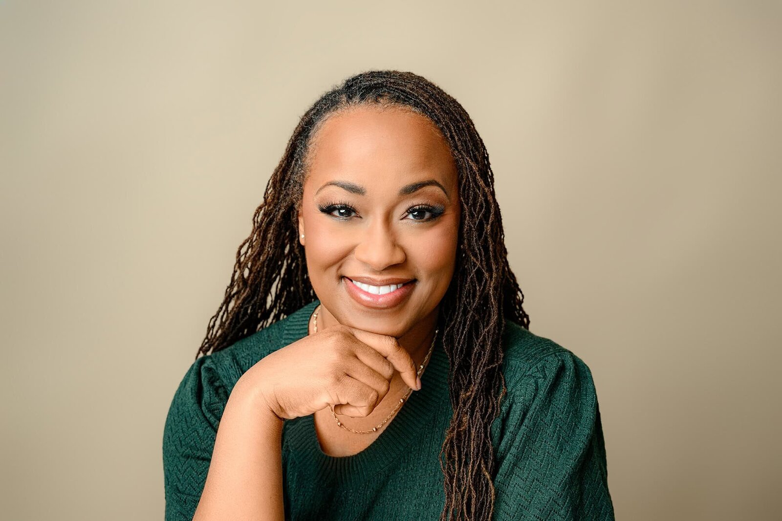 dark hair woman wearing a green sweater against a brown background for headshot
