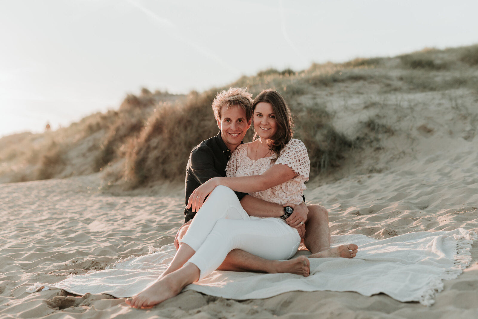 Couple cuddle together on a cosy cream blanket on the soft sandy beach at Camber Sands