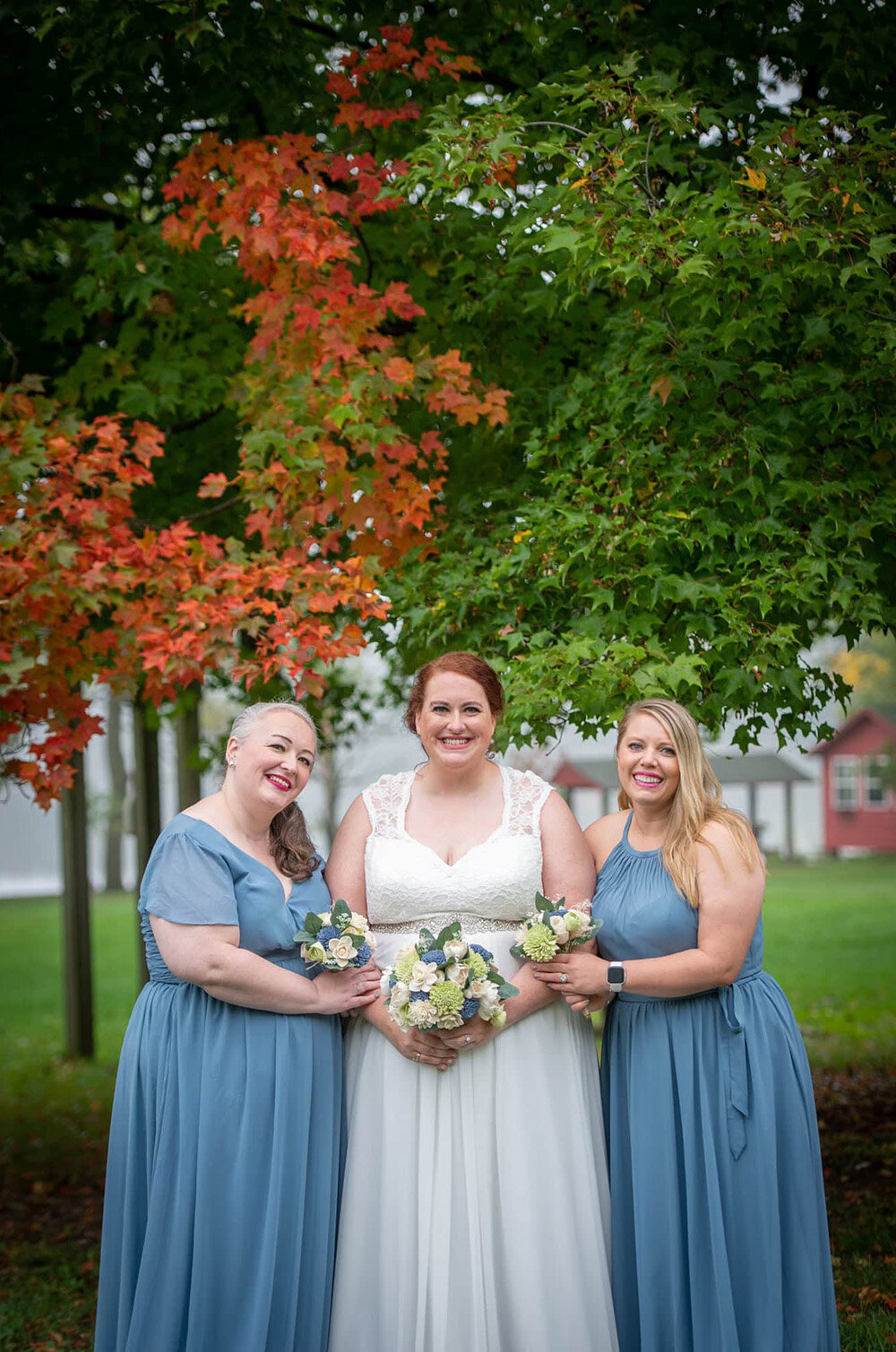 bride with bridesmaids in blue in front of fall and summer colors