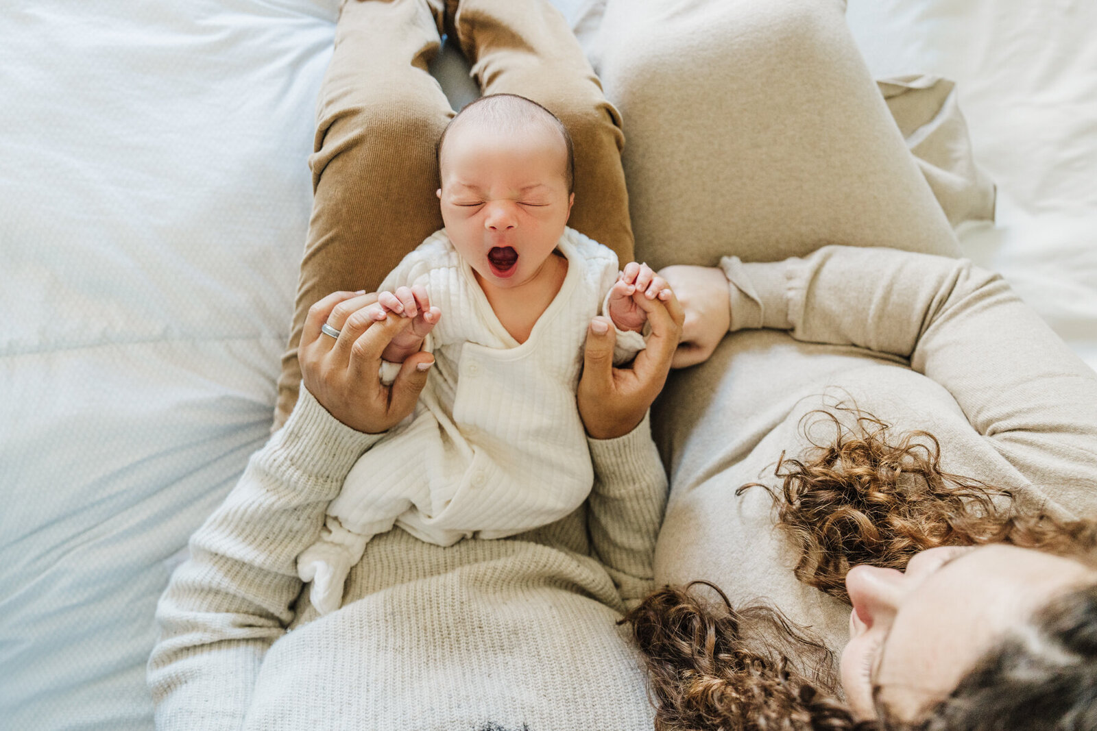 baby in parents lap yawns at camera during boston newborn photoshoot