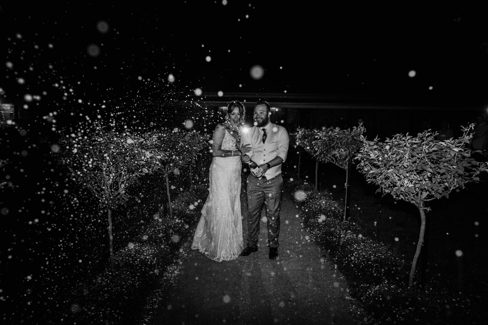 Black and white photo of a couple popping champagne at night with bubbles everywhere
