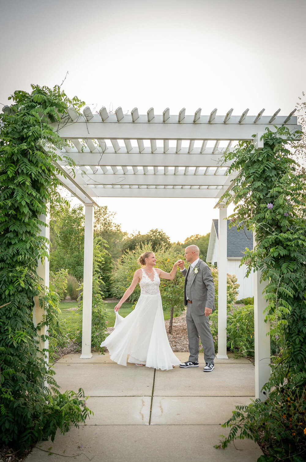 groom holds bride's hand under trellis as she swishes dress