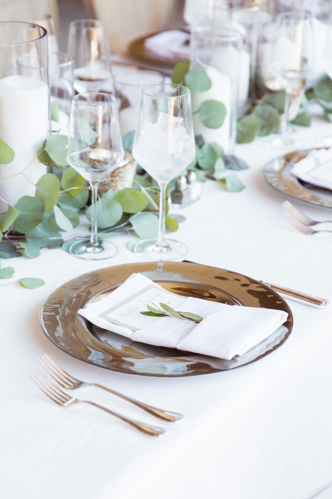 Elegant dinner plate with utensils, glasses and green centerpieces