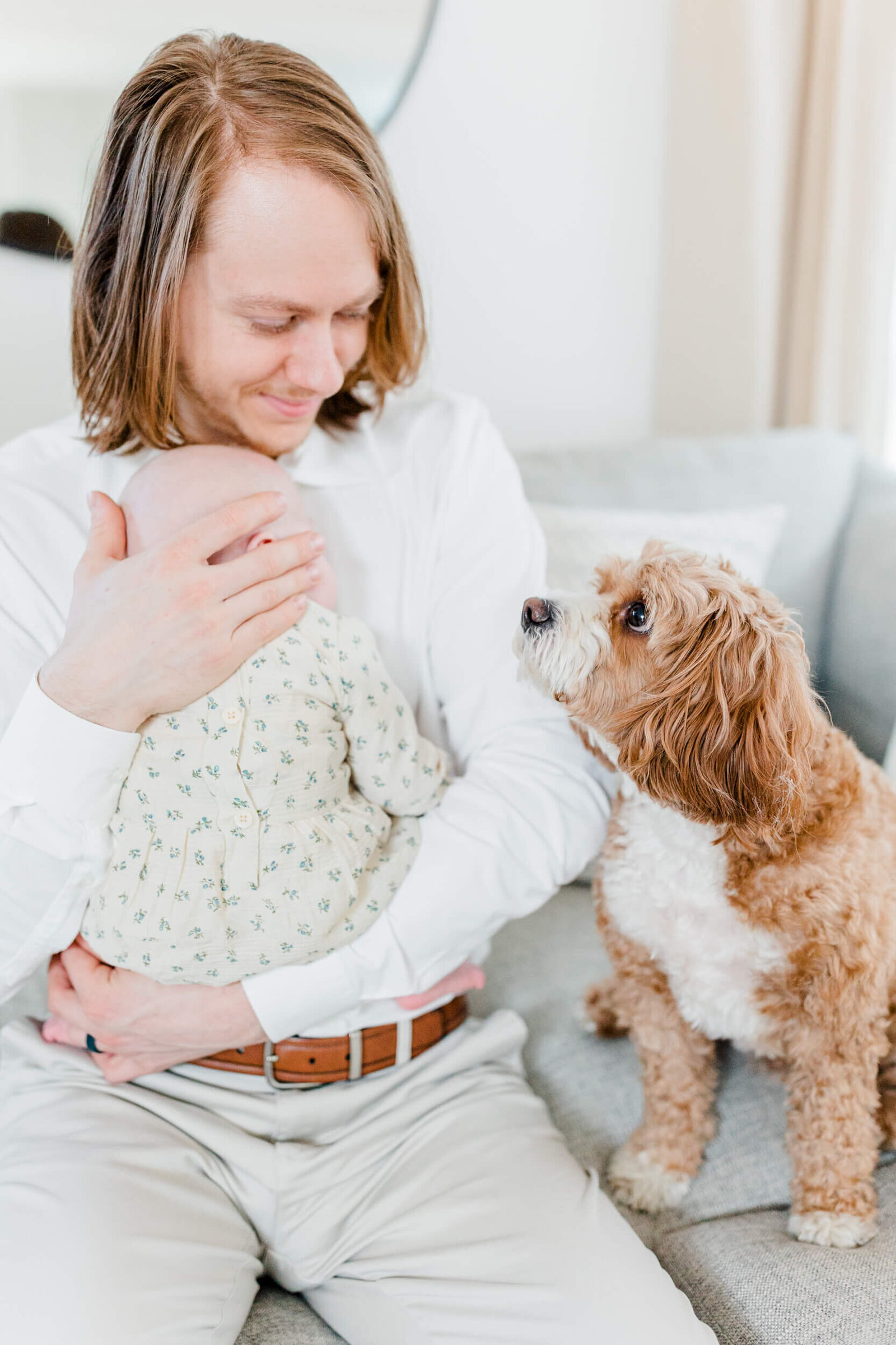 Dad holds newborn and smiles at curious dog