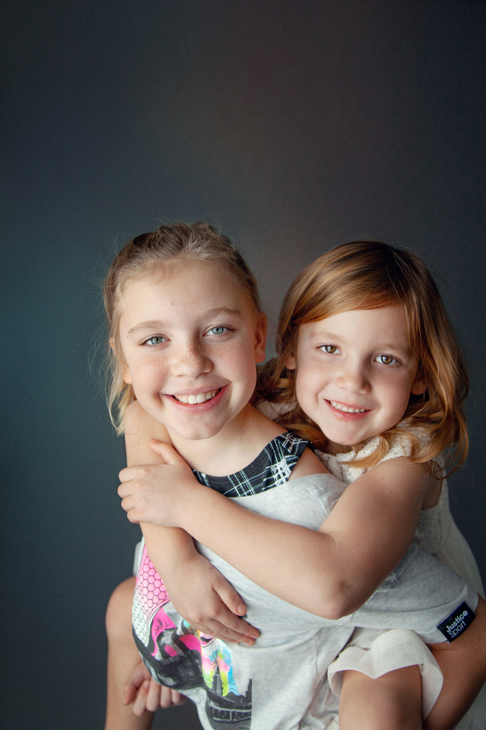 Sisters piggy back with gray background.