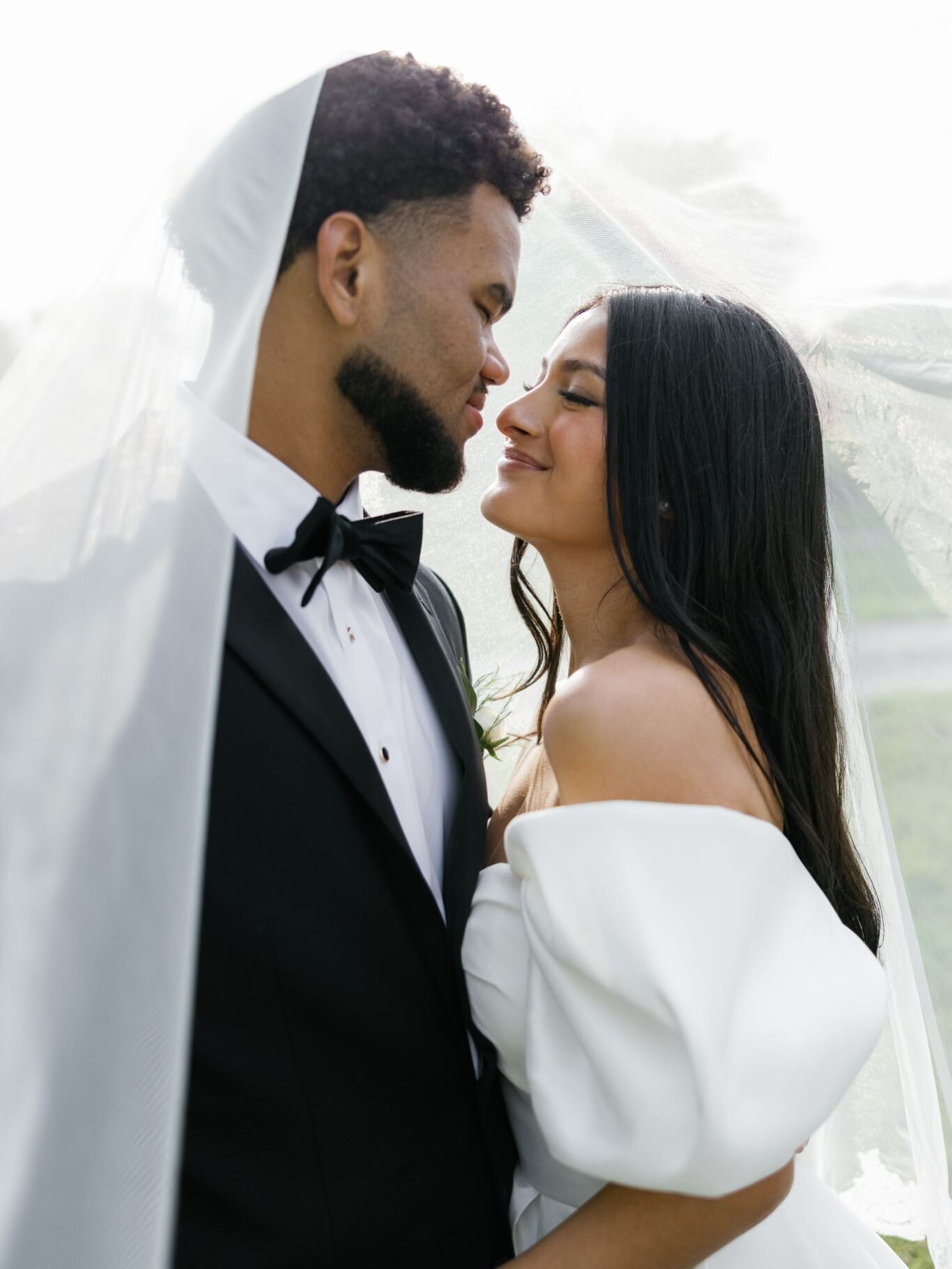 Bride and groom smiling under the veil, sharing a quiet, intimate moment.