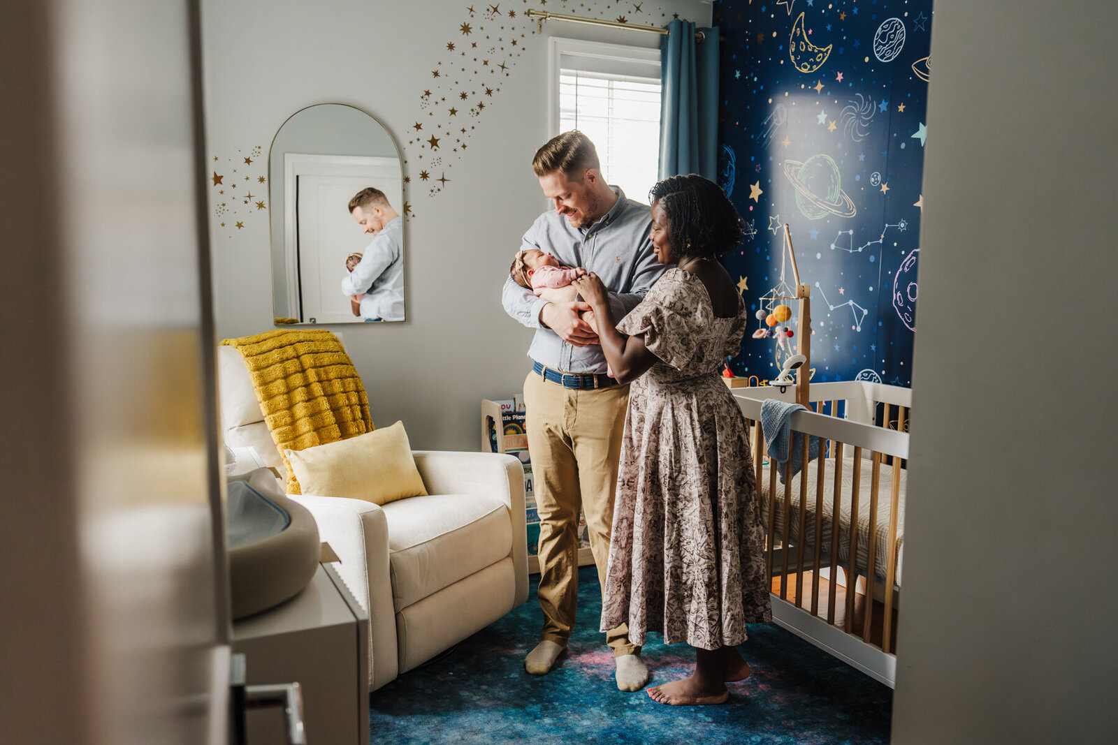 two parents stand holding infant daughter in a nursery with a star and space theme