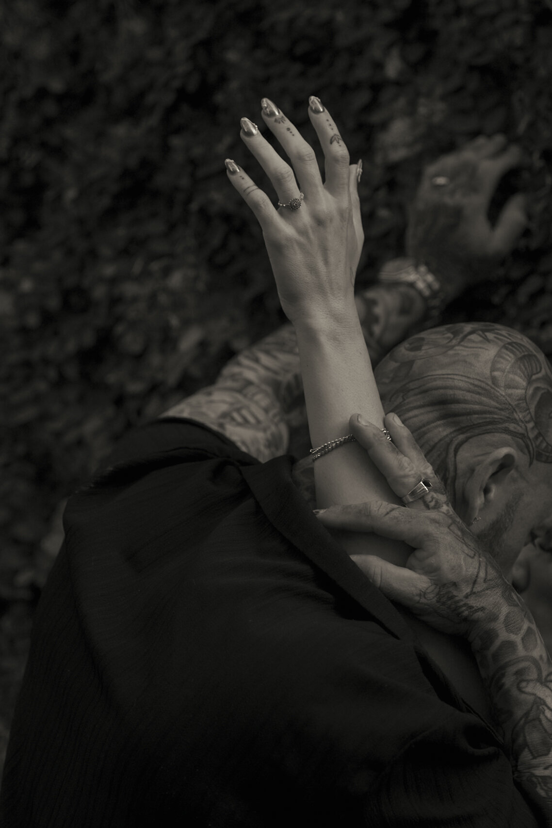 Artistic black and white photo of tattooed lovers, featuring detailed hand and ring composition.