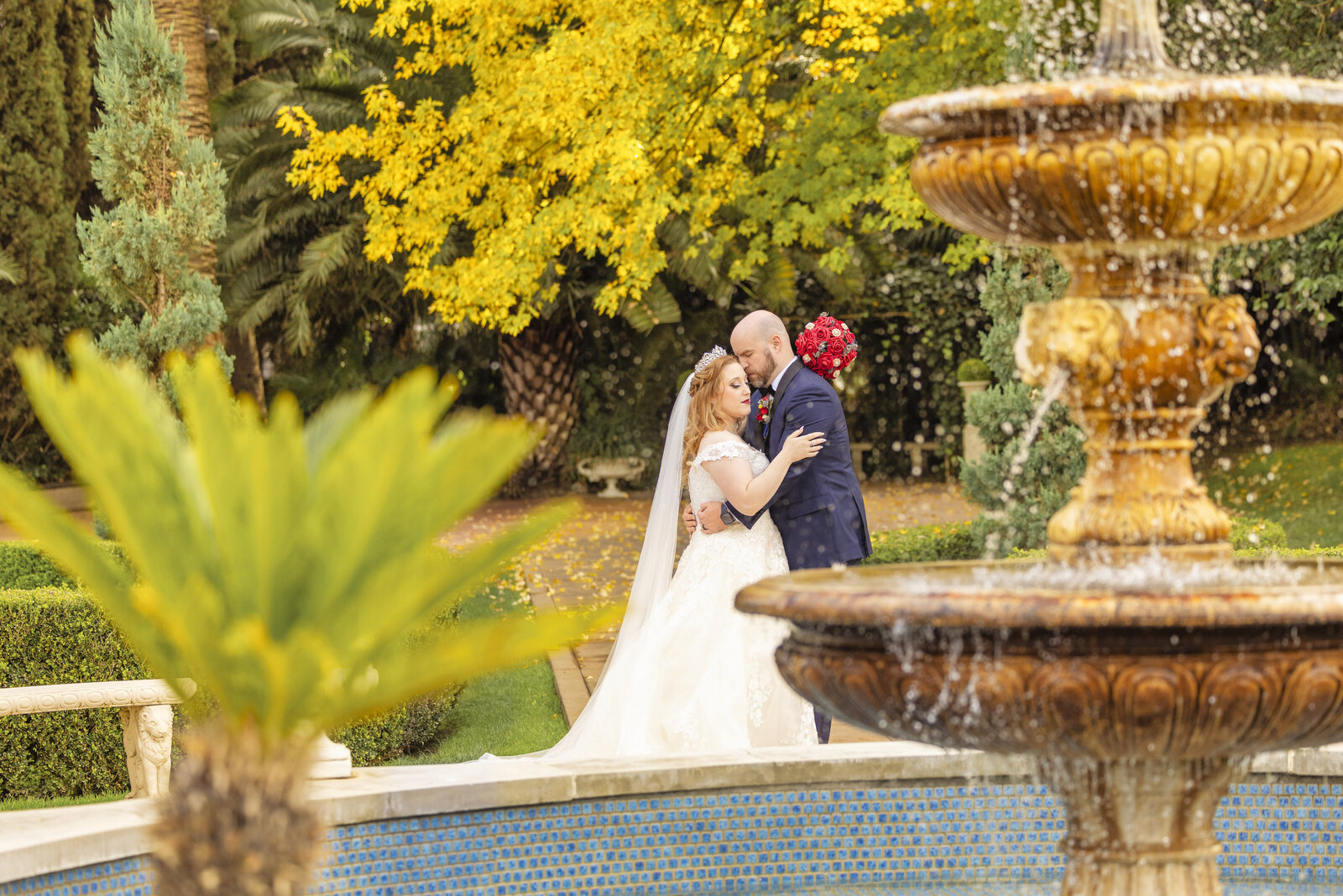 Bride and groom embrace at Grand Island Mansion behind a water fountain for couples portraits at a Sacramento area wedding.