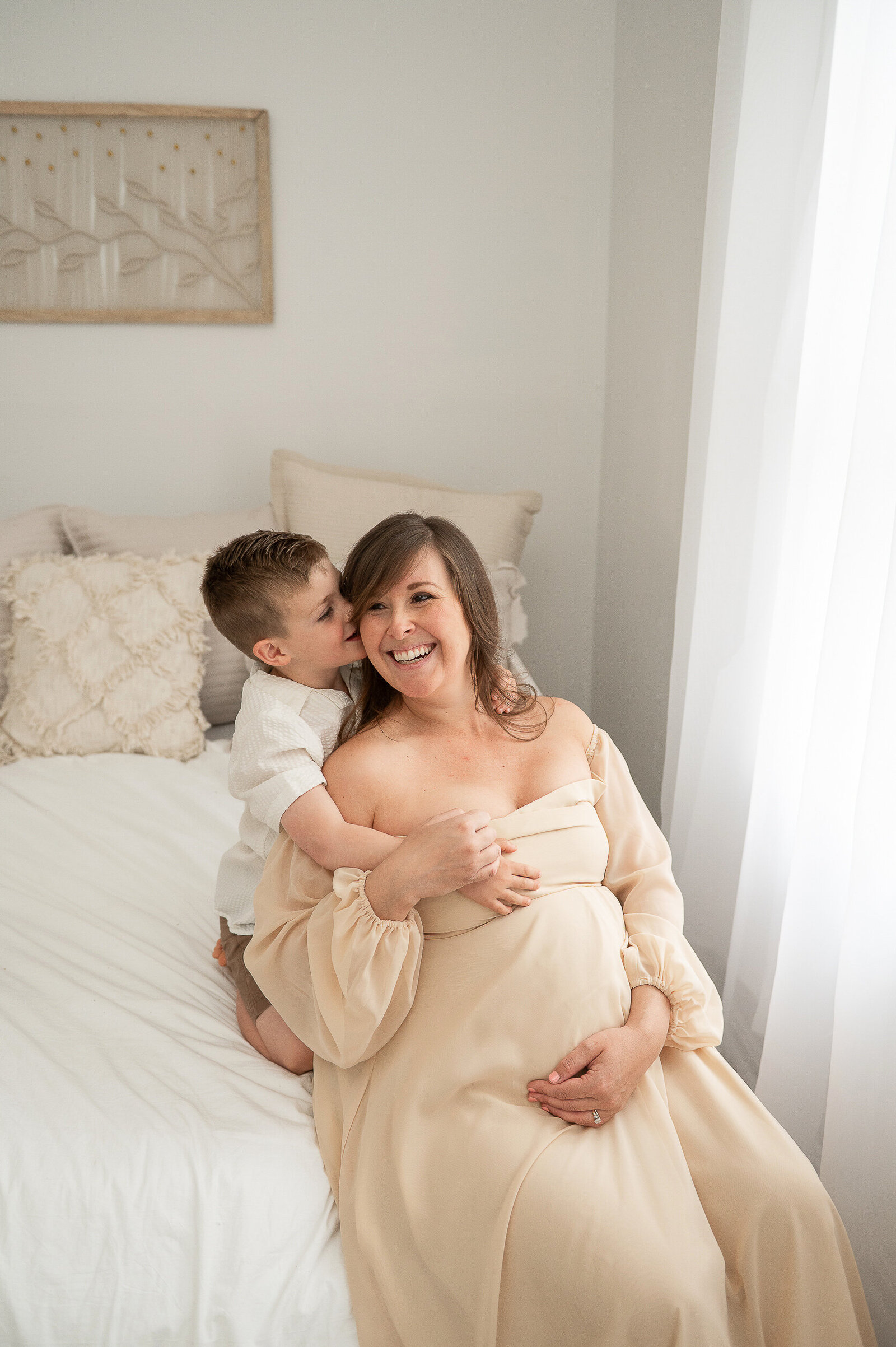 Joyful maternity photo of a mother holding her baby bump, embracing her young son in a warm Baltimore studio setting.