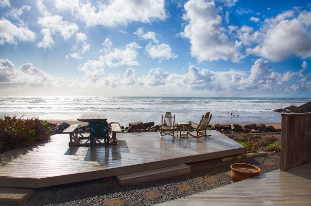 A view of the ocean from a coastal beach with a deck and wood chairs.