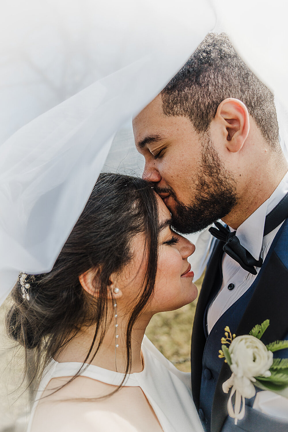 groom kisses bride on forehead under veil