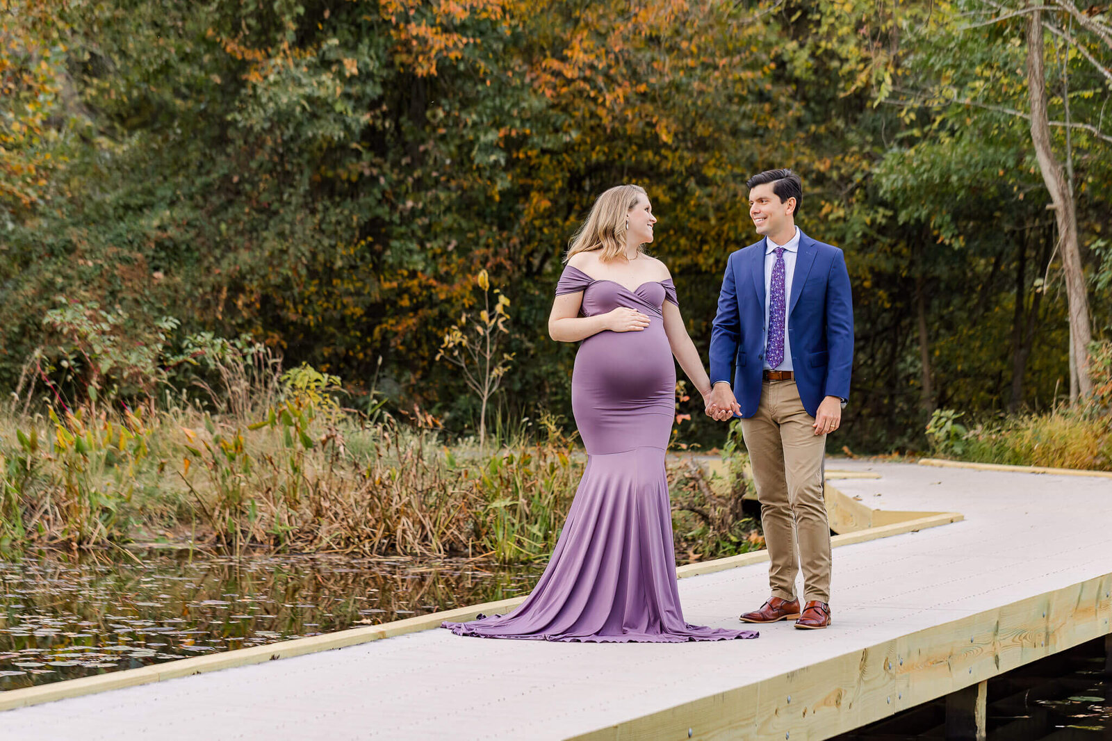 A pregnant couple walking across a bridge at a park.