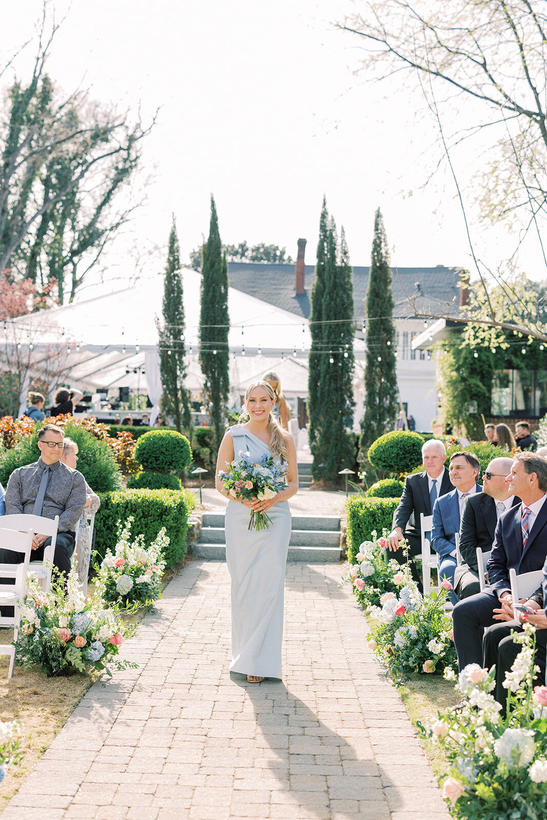 bridesmaid walks down the aisle holding bouquet in blue dress