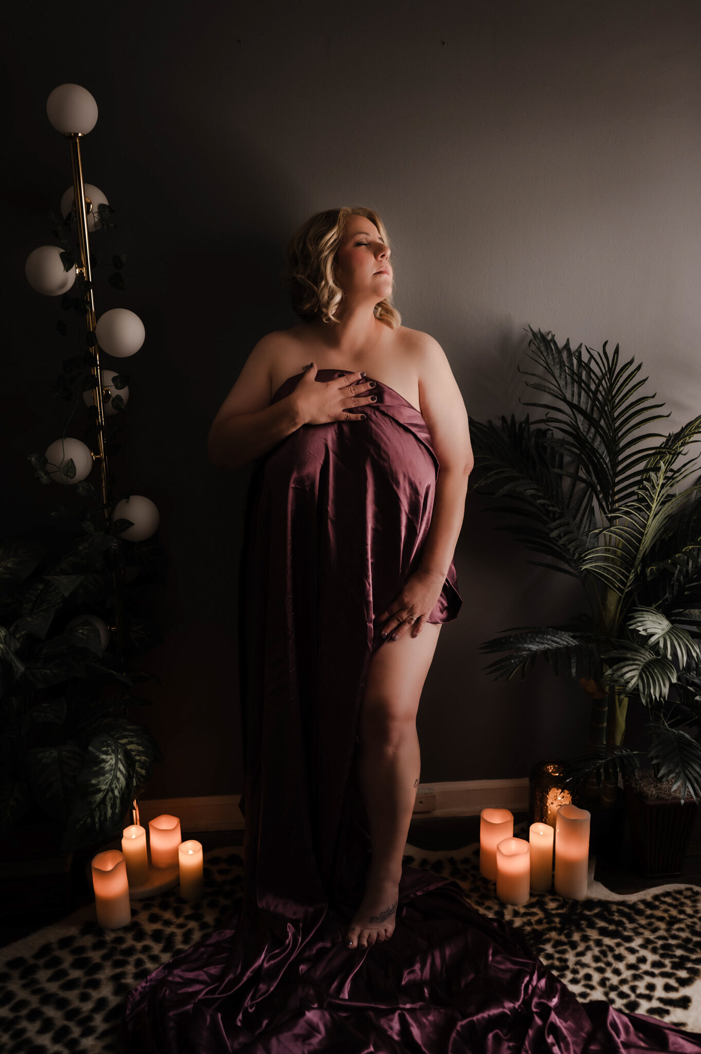 A woman stands in a boudoir studio covered in a purple sheet