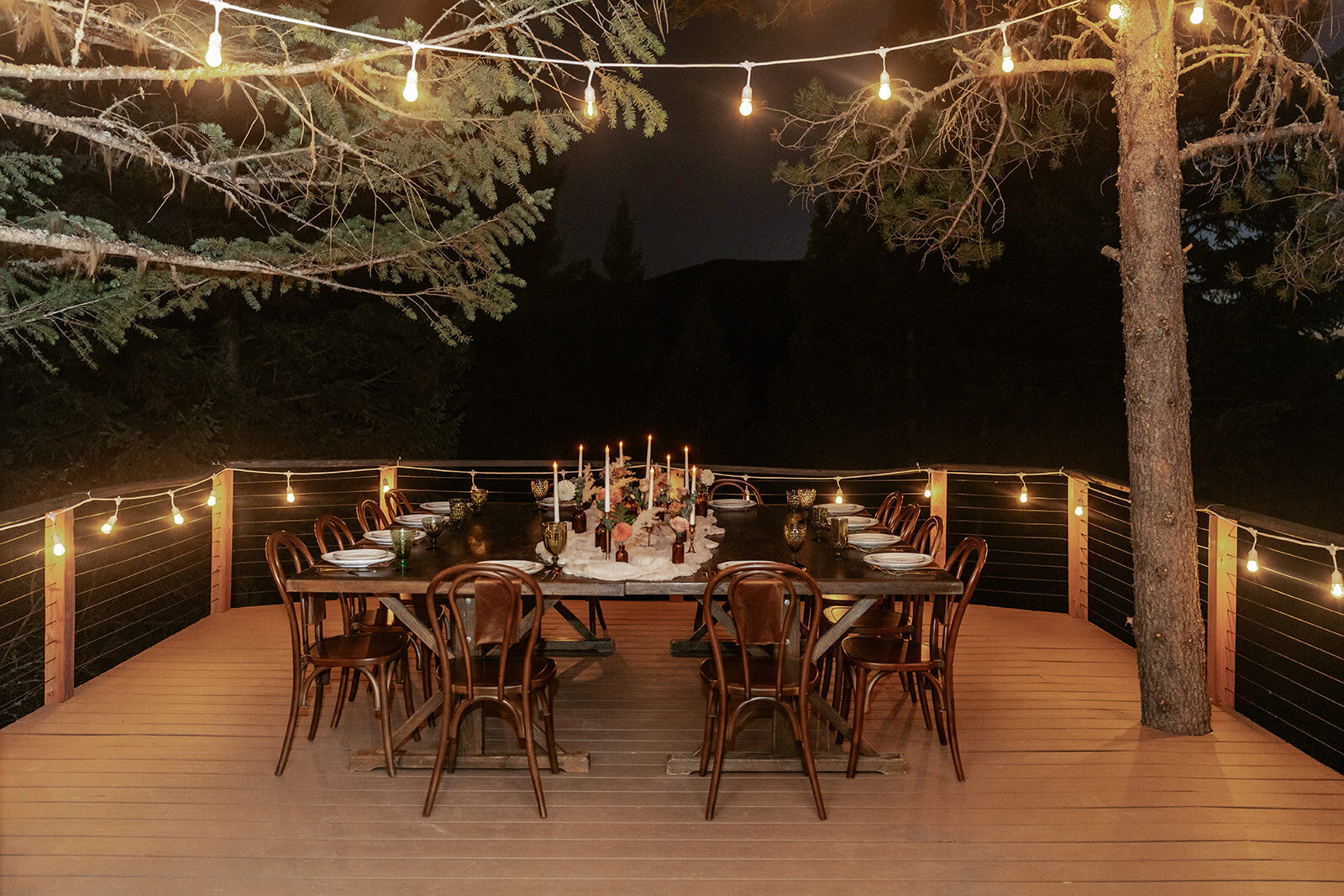 A cozy evening elopement dinner under string lights with a candlelit table surrounded by trees and mountain air.