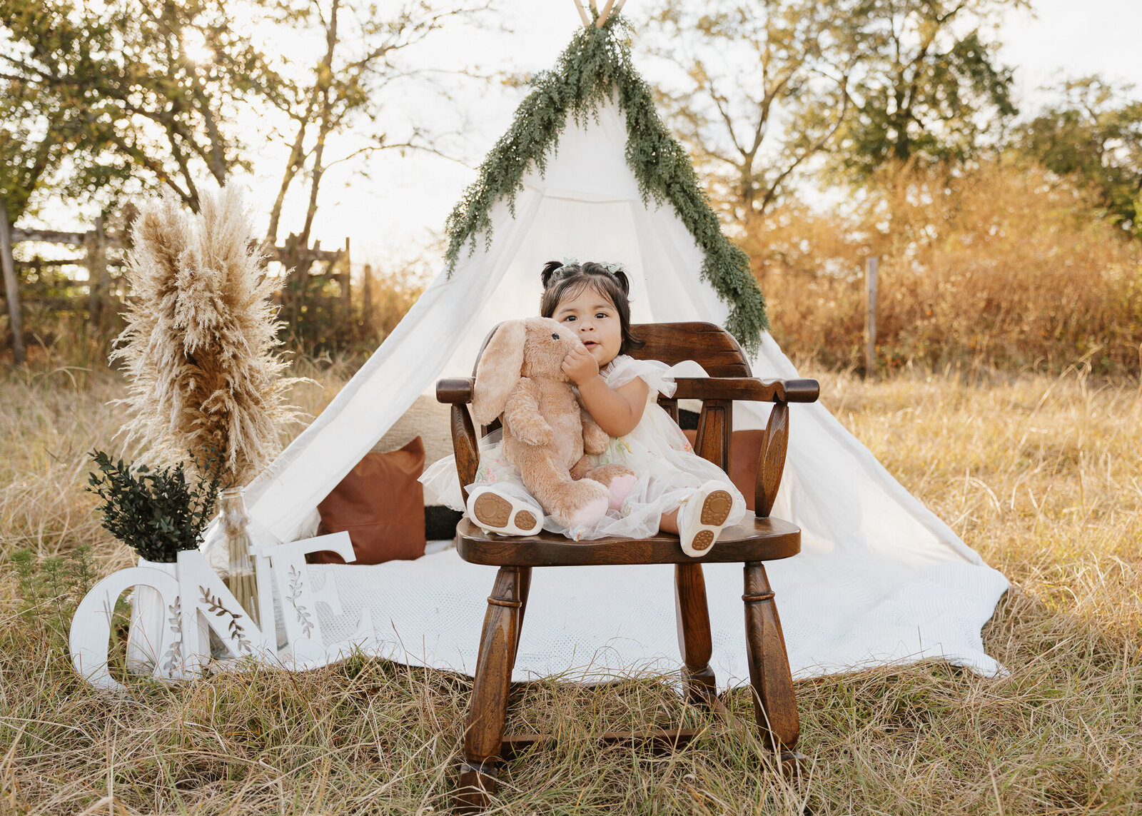 Boho first birthday session in Aiken SC - baby girl sitting inside a styled teepee with pampas grass in a warm fall field.