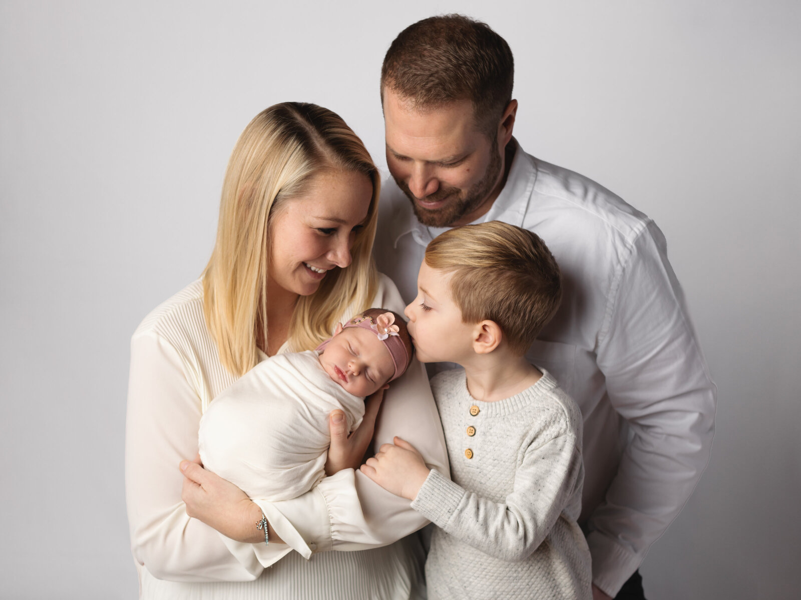 mom and dad holding newborn baby girl while brother kisses forehead for studio portraits