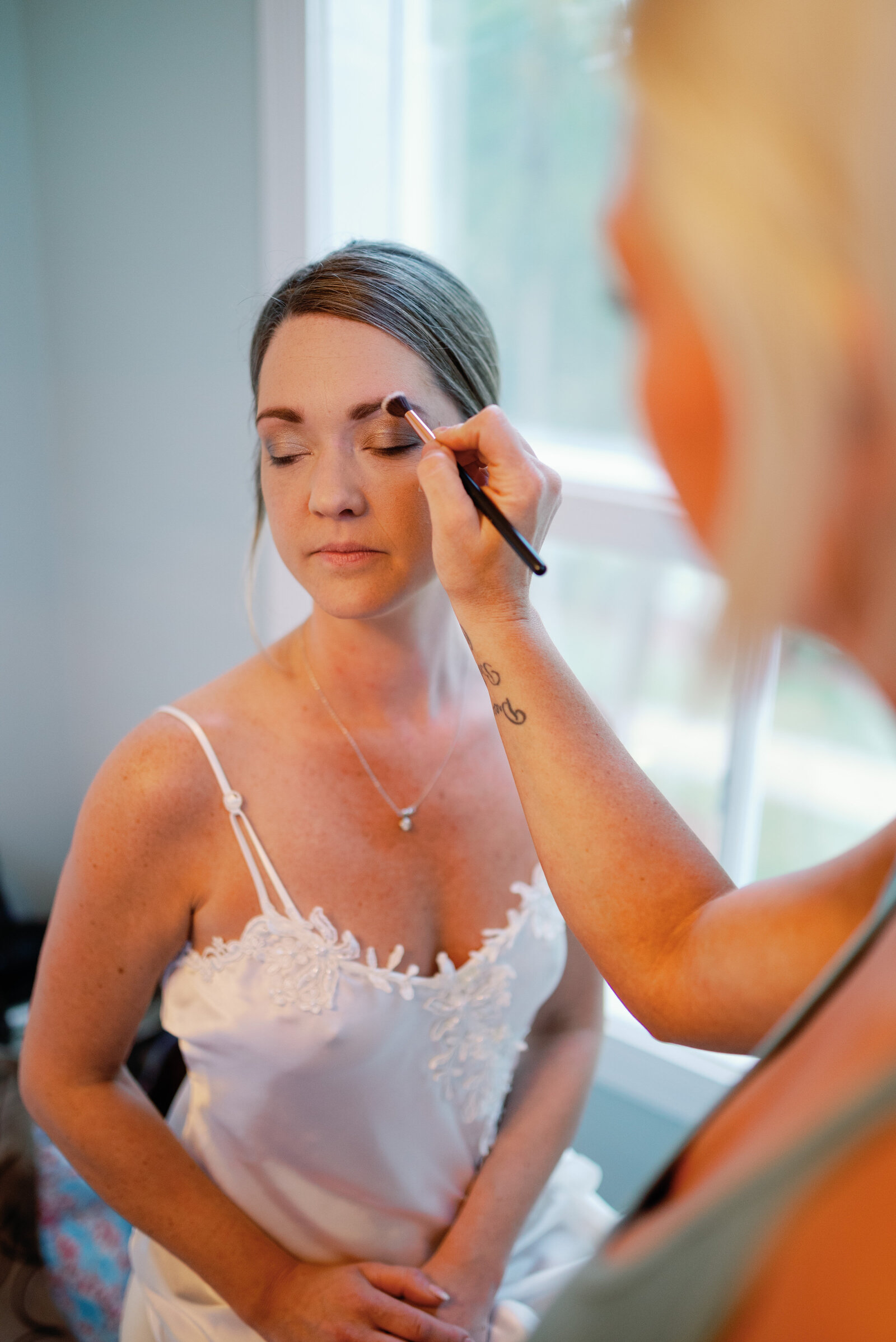 bride sitting with her eyes closed while she is getting her makeup applied for her wedding day