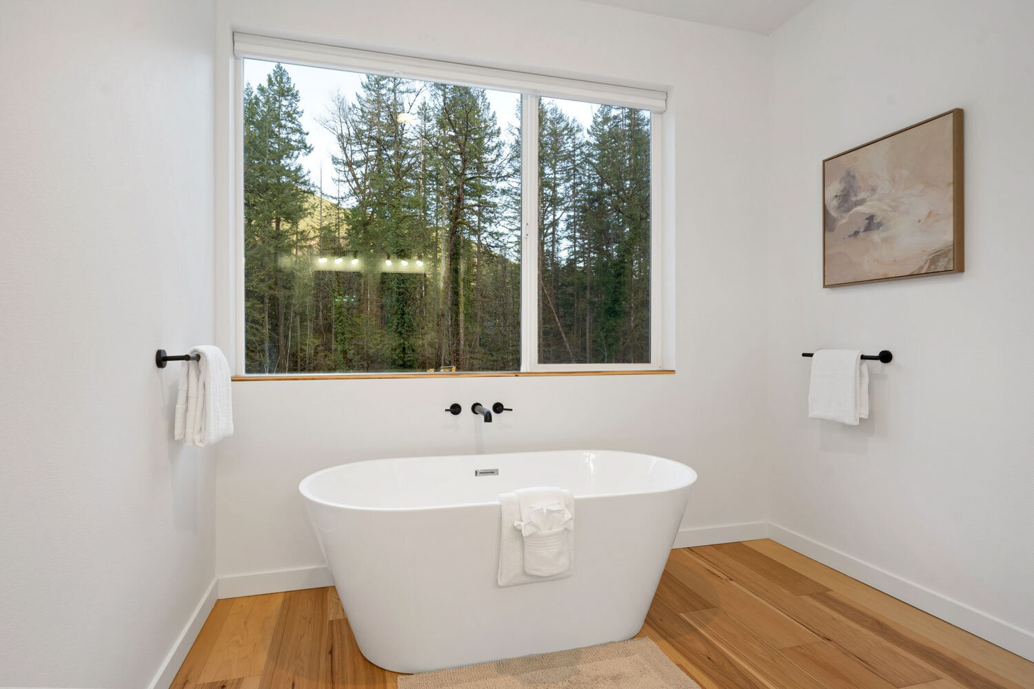 White freestanding bathtub in front of a large window with forest view