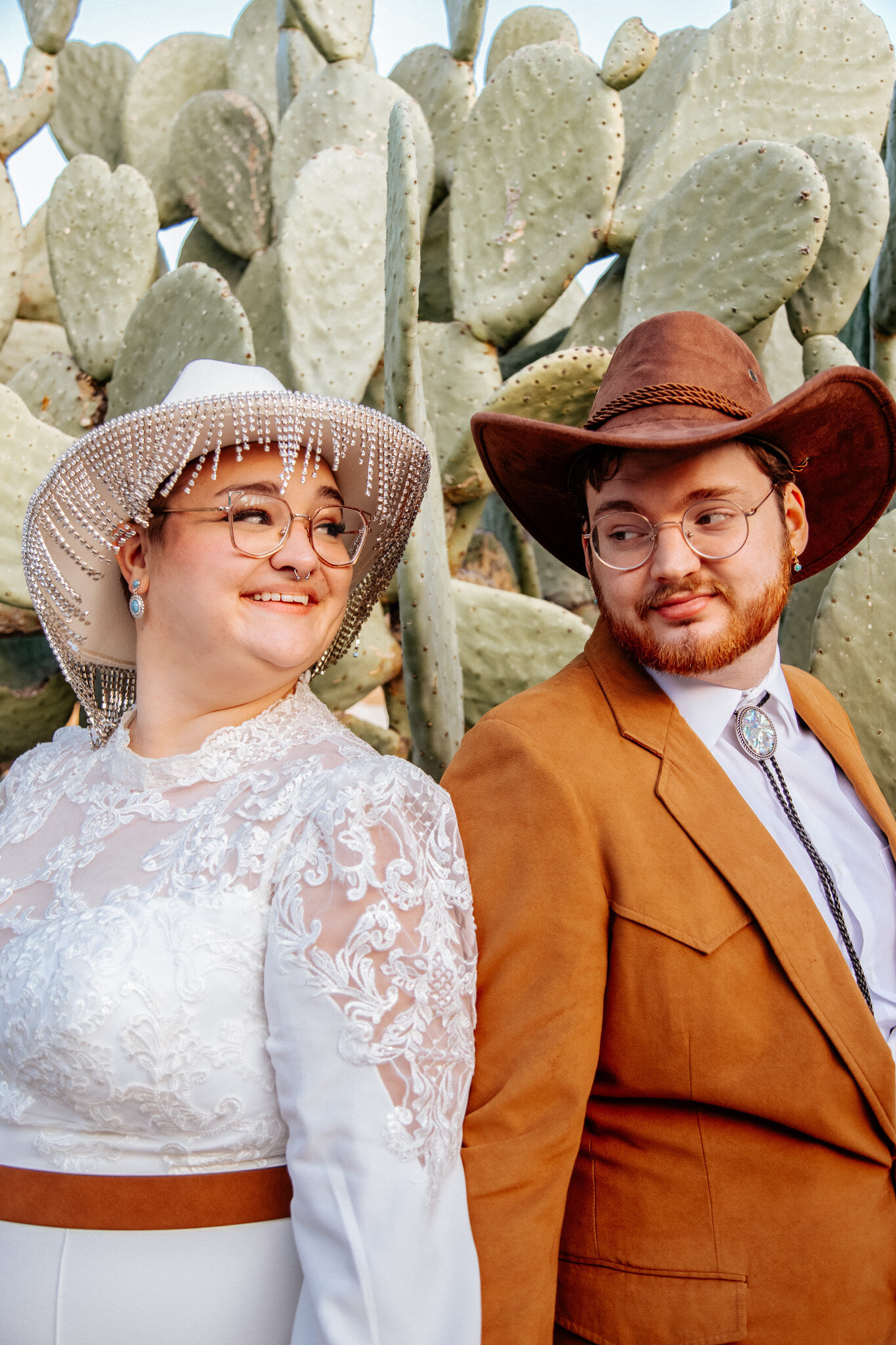 non-binary couple stands back to back infront of arizona cactus at wedding