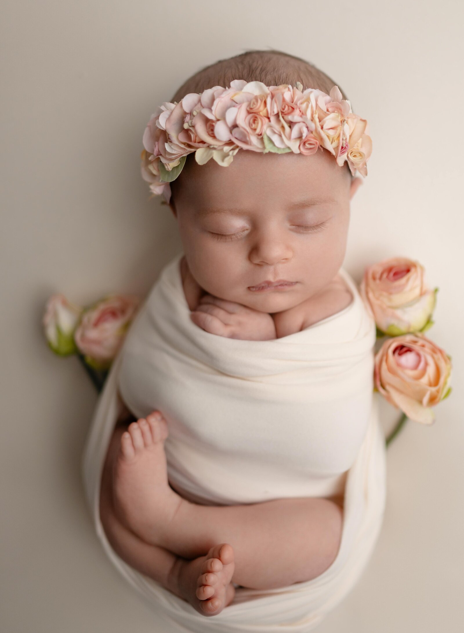 Baby girl swaddled in a cream wrap with peach roses by her side.