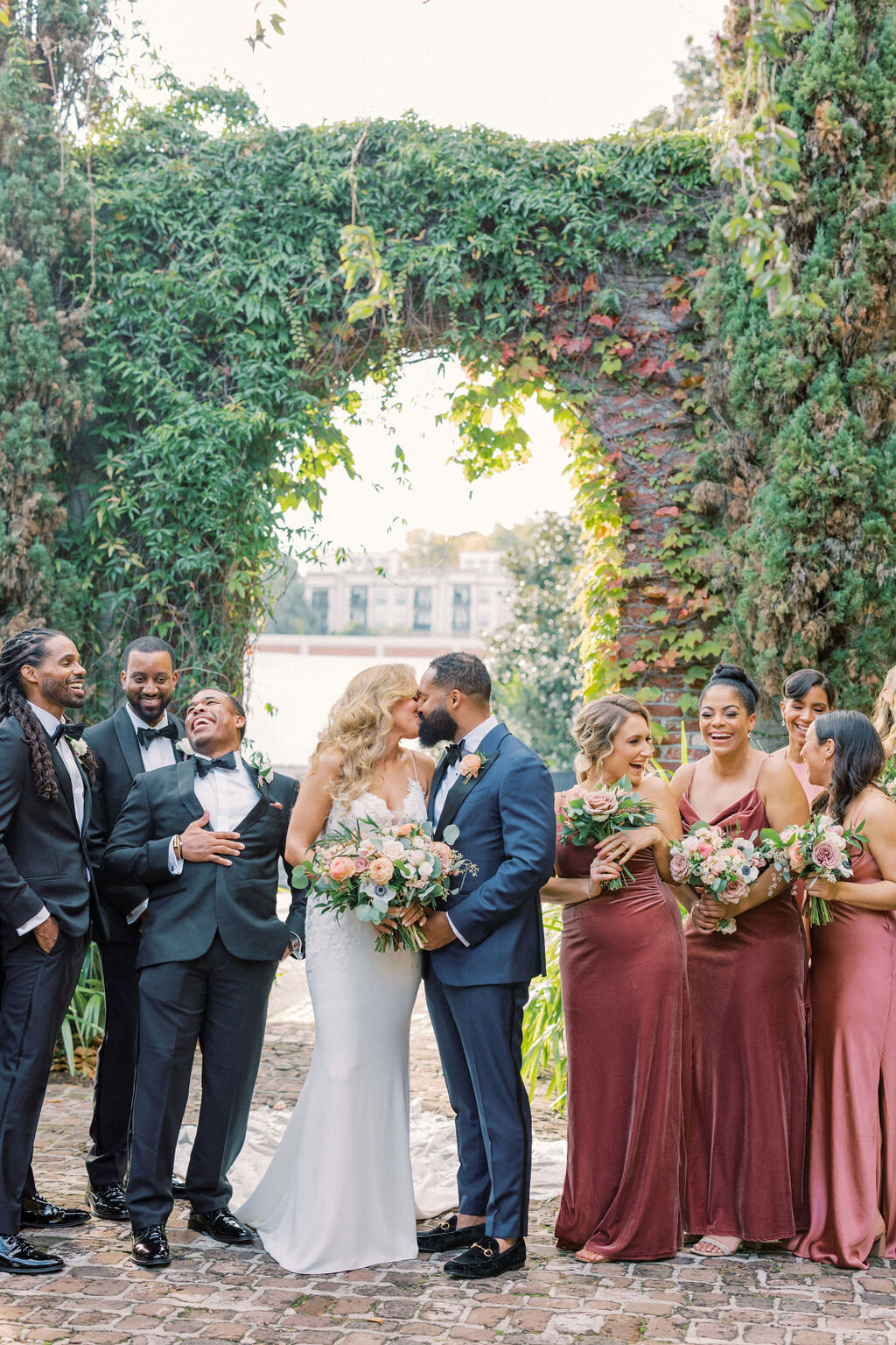 Bride kisses groom while bridal party cheers outside of Summerour Studio ivy brick archway