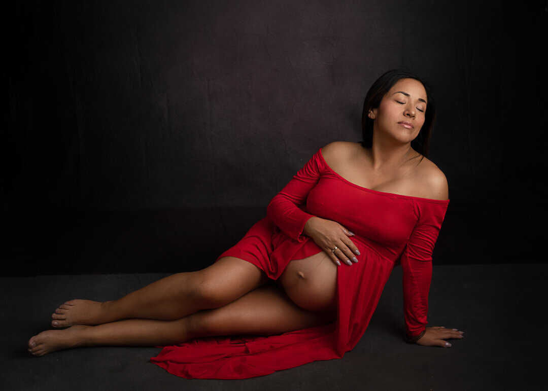 maternity mom wearing red dress against a black background