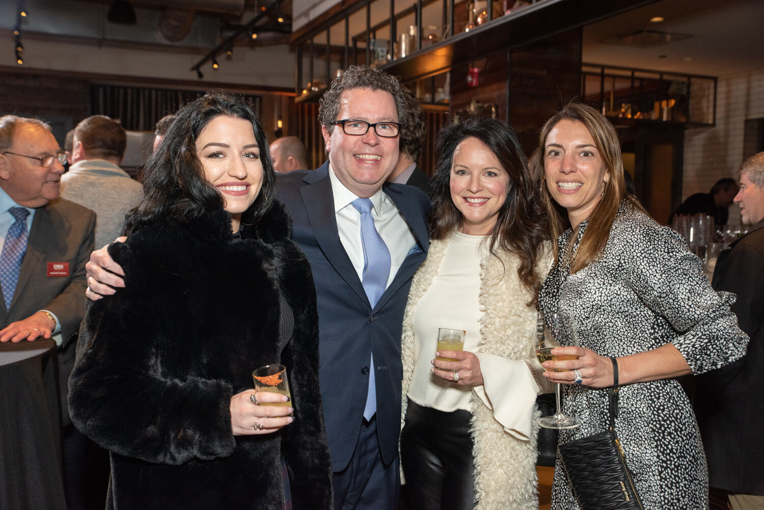 Group of four people dressed for an evening event, smiling with drinks in hand