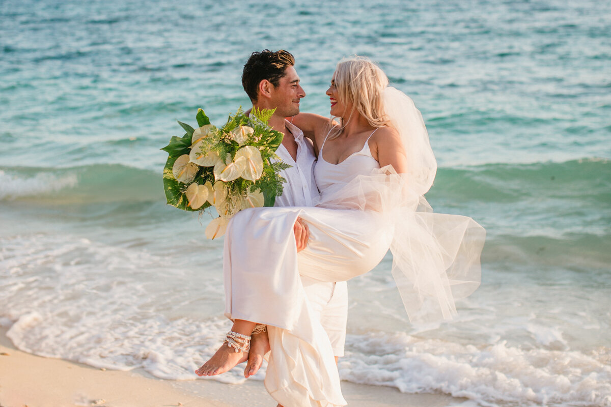 groom carrying bride in his arms on the beach