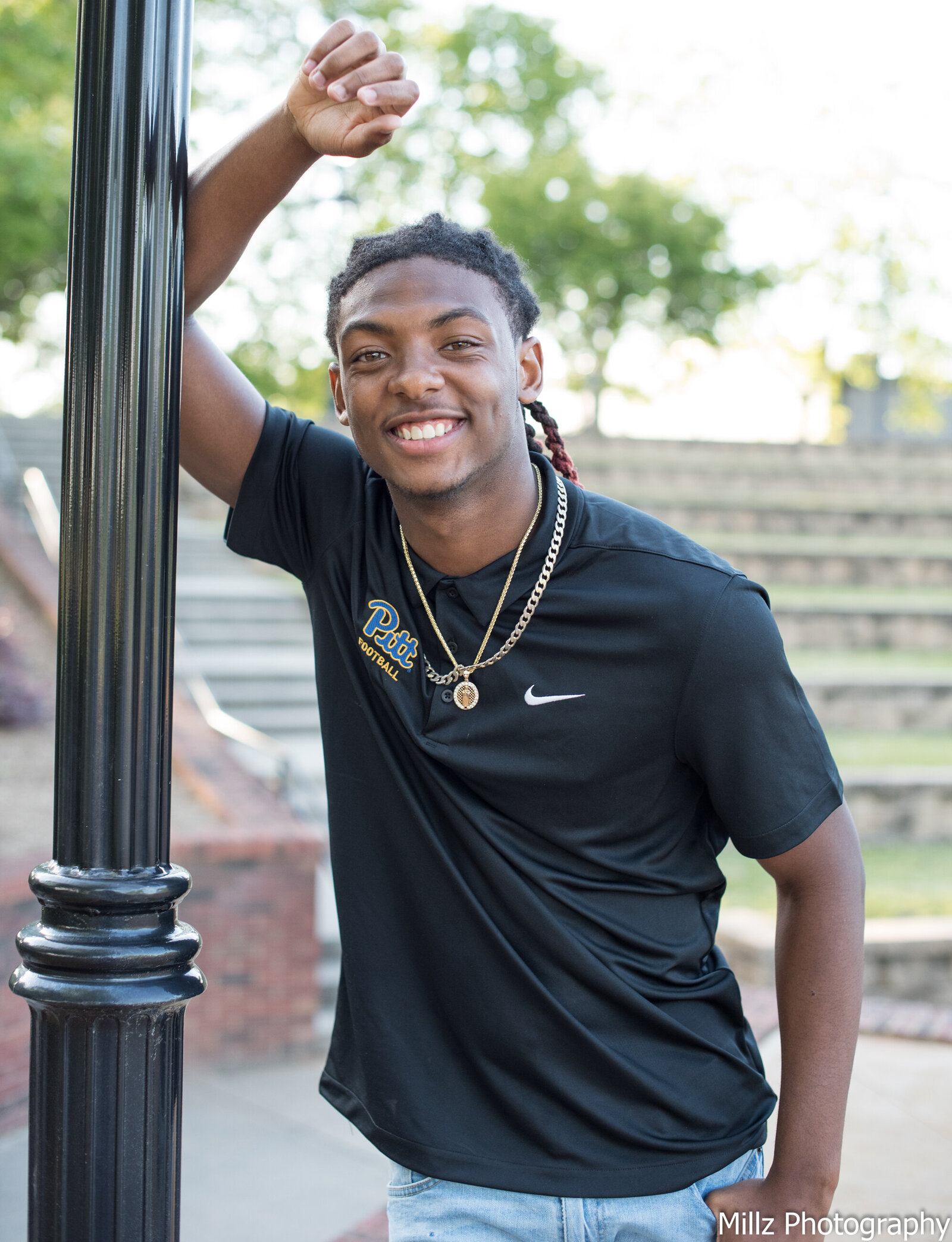 a senior dressed in a black nike shirt leaning against a light pole as he poses for his graduation photos. photographed by Millz Photography in Greenville, SC