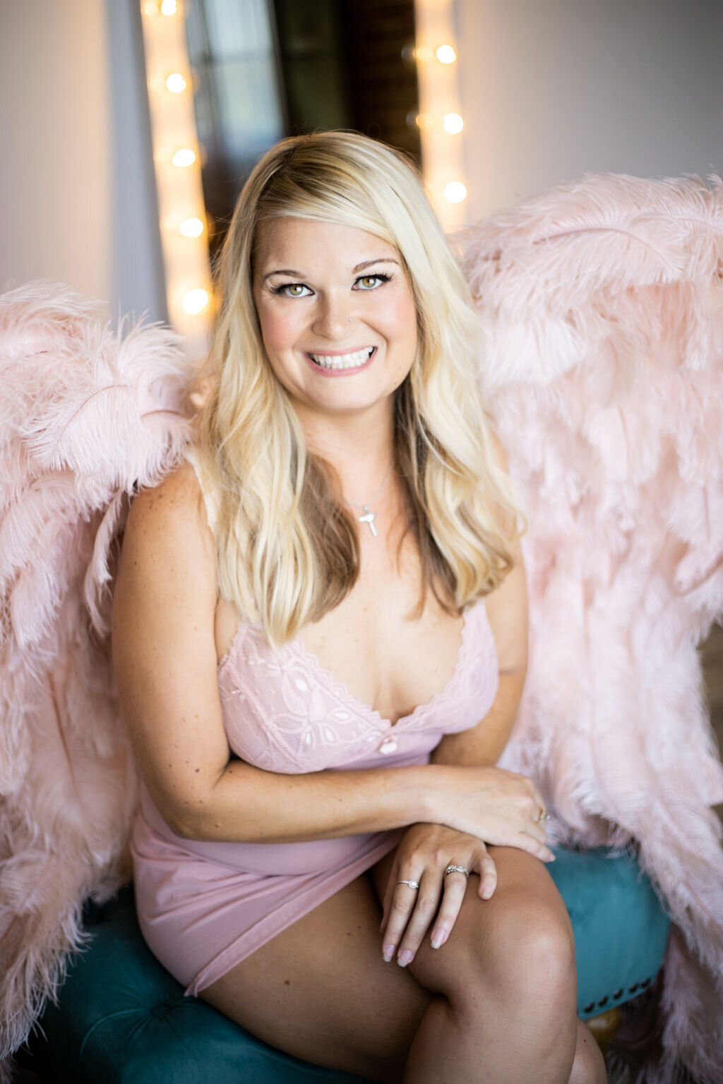 woman posed sitting cross legged in studio with pink wings and lingerie