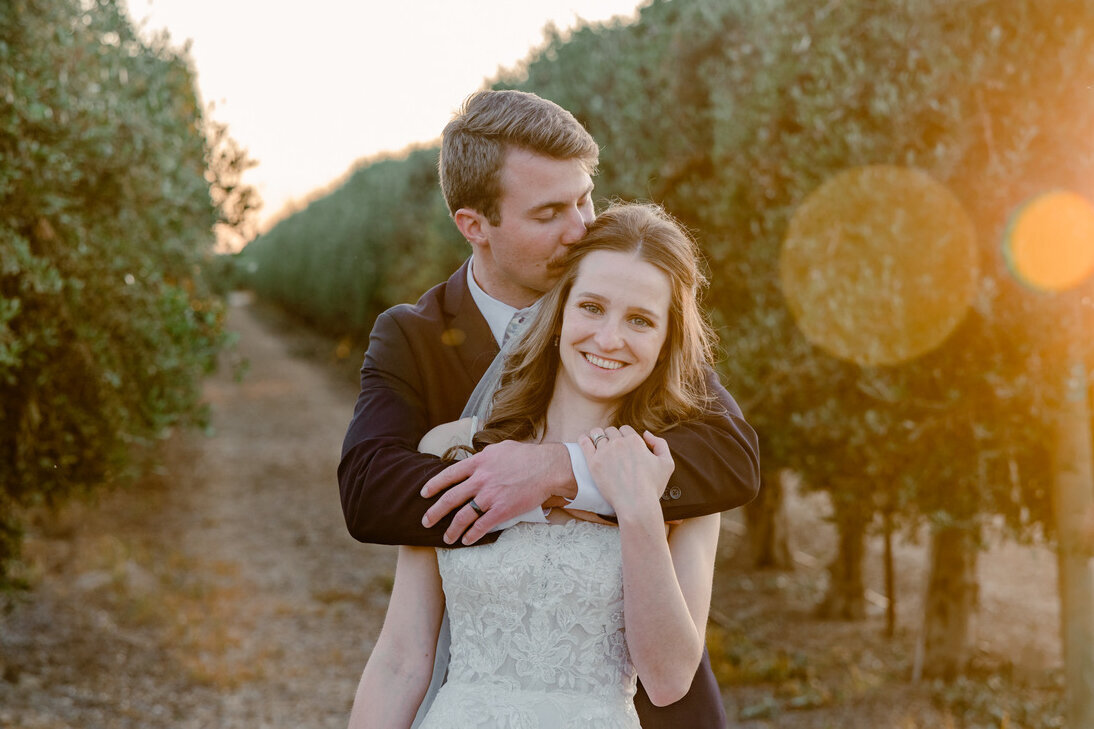 groom hugging bride from behind in golden sun