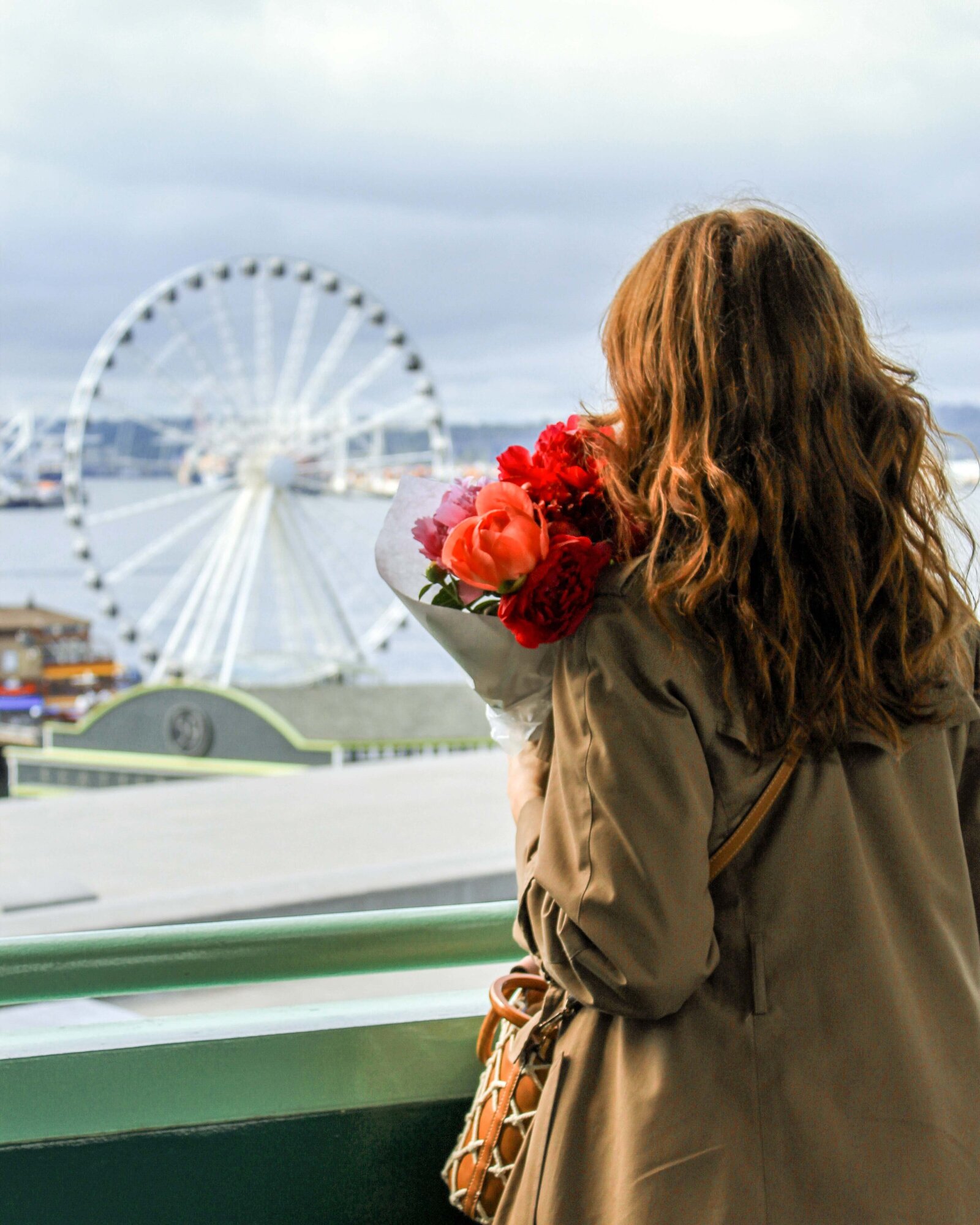 Nicole Moore girl in Trench coat with flowers at Pike Place Market overlooking ferris wheel in Seattle