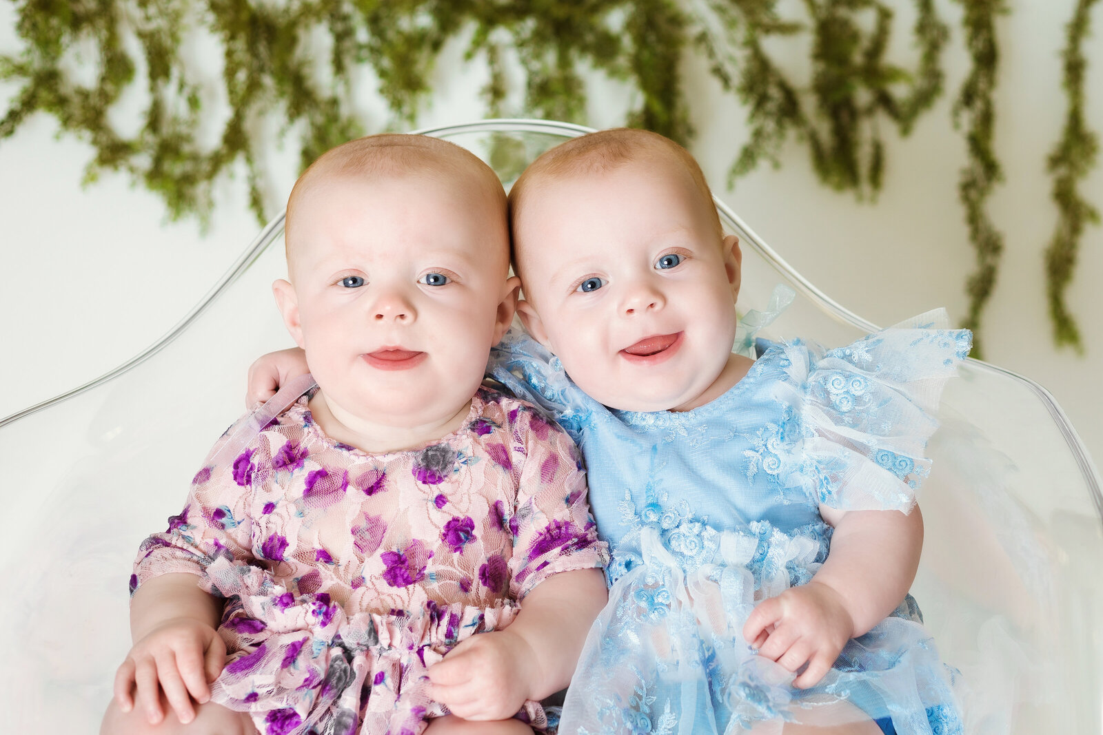 Milestone Photographer, a two baby girls sits beside each other in dresses, one has an arm around the other