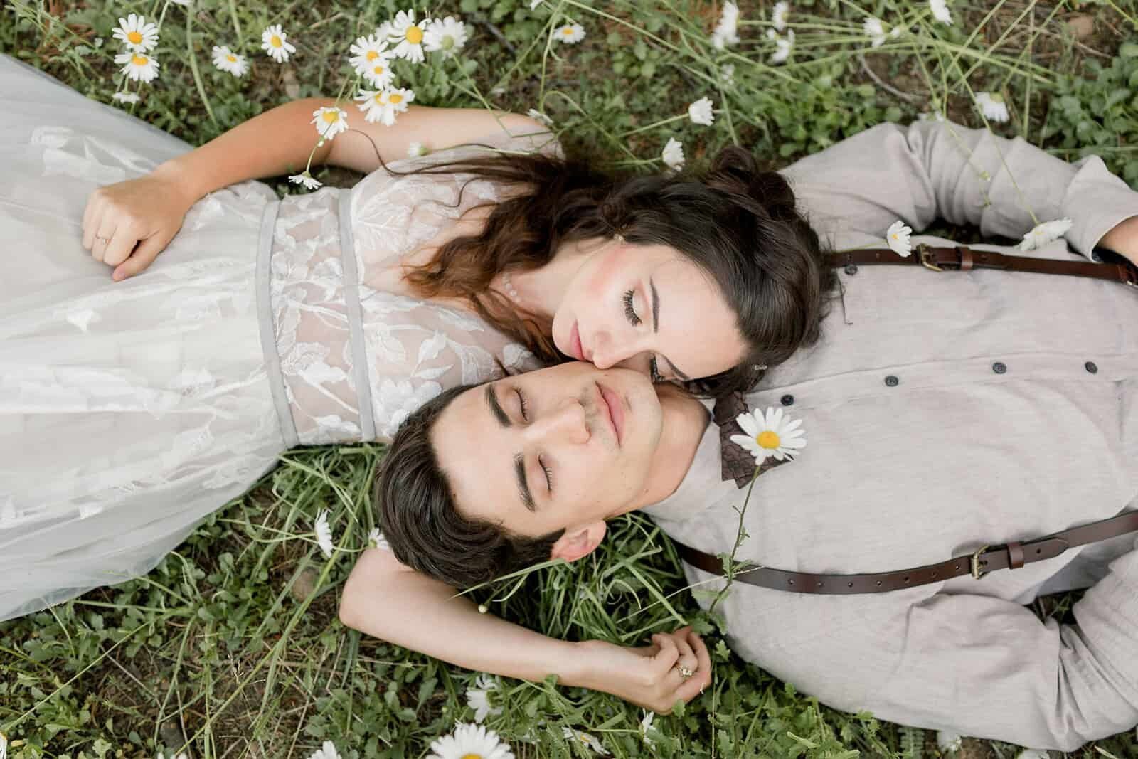  A bride and groom lay in a meadow with daisies on their wildflower wedding. 