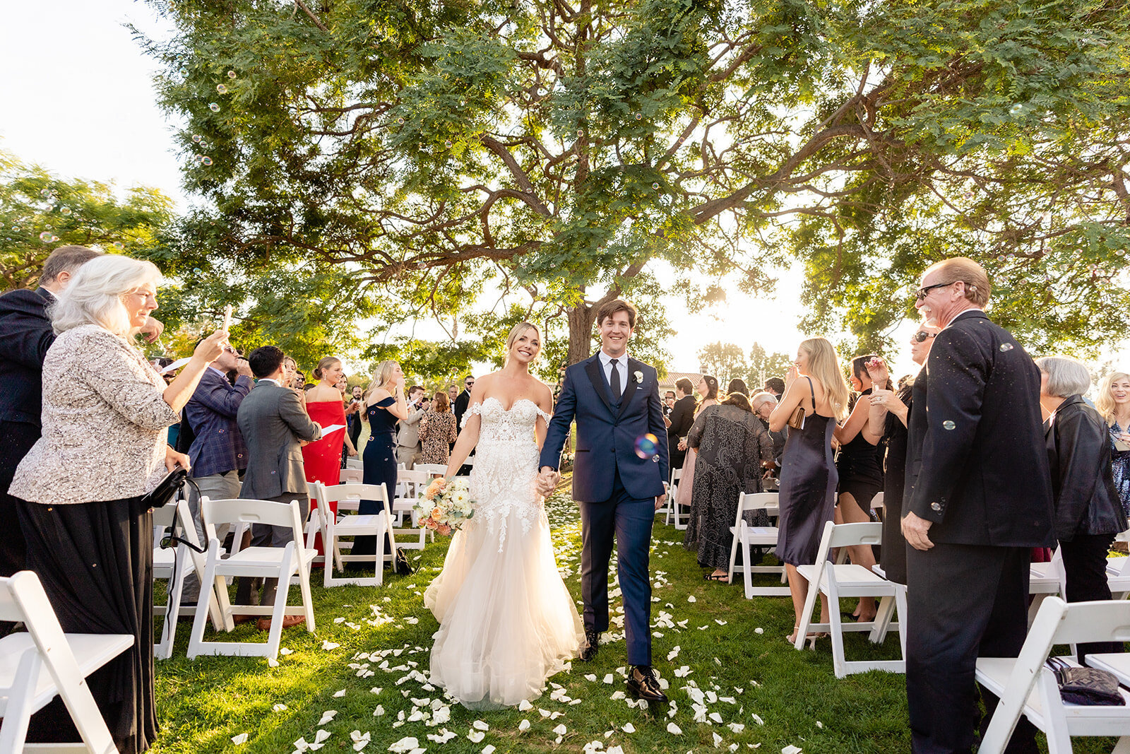 A bride and groom holding hands walking back down the aisle after getting married with their guests standing and applauding at The Inn at Rancho Sante Fe