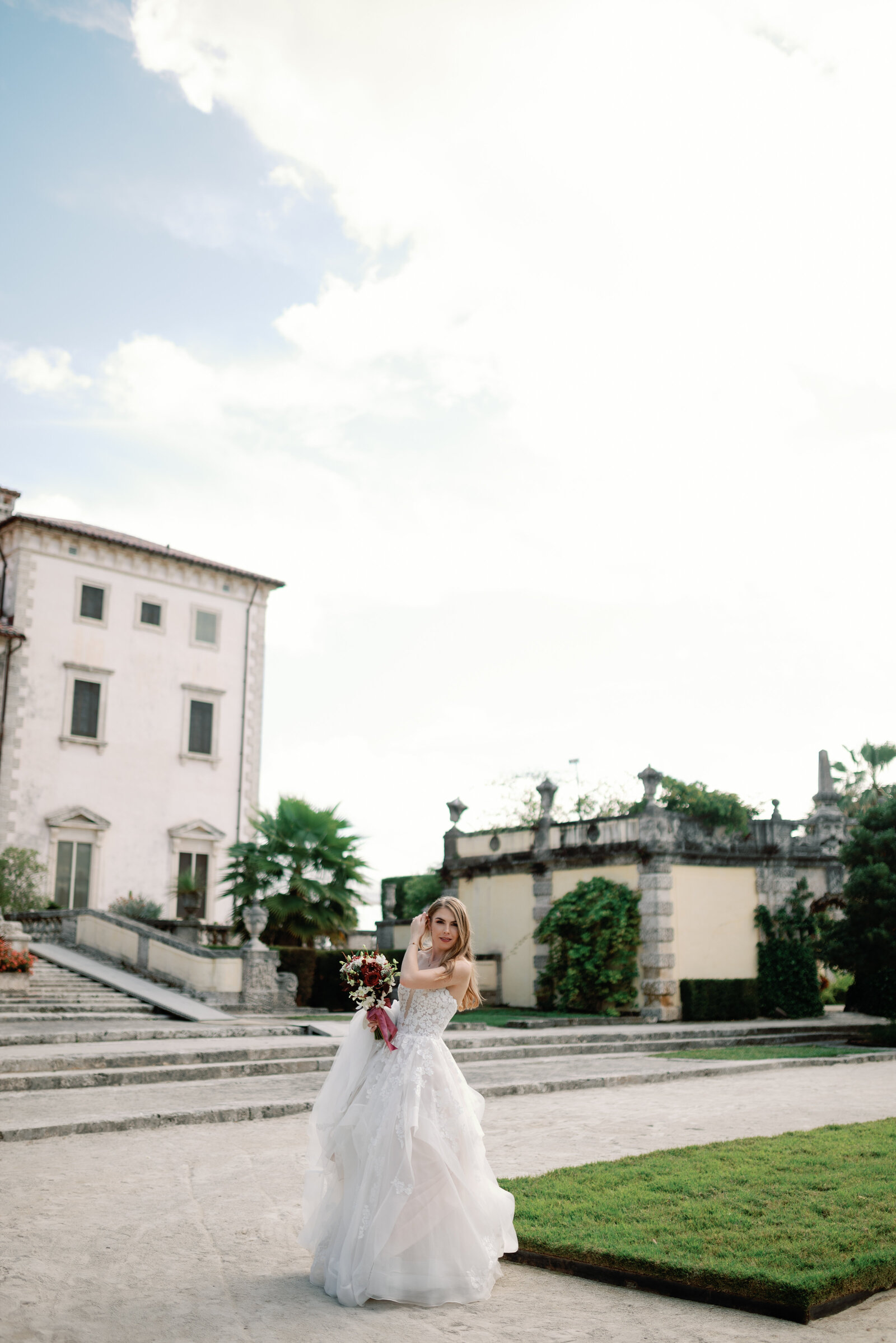 Bride stopping to fix her hair while walking across Vizcaya gardens to the ceremony location.