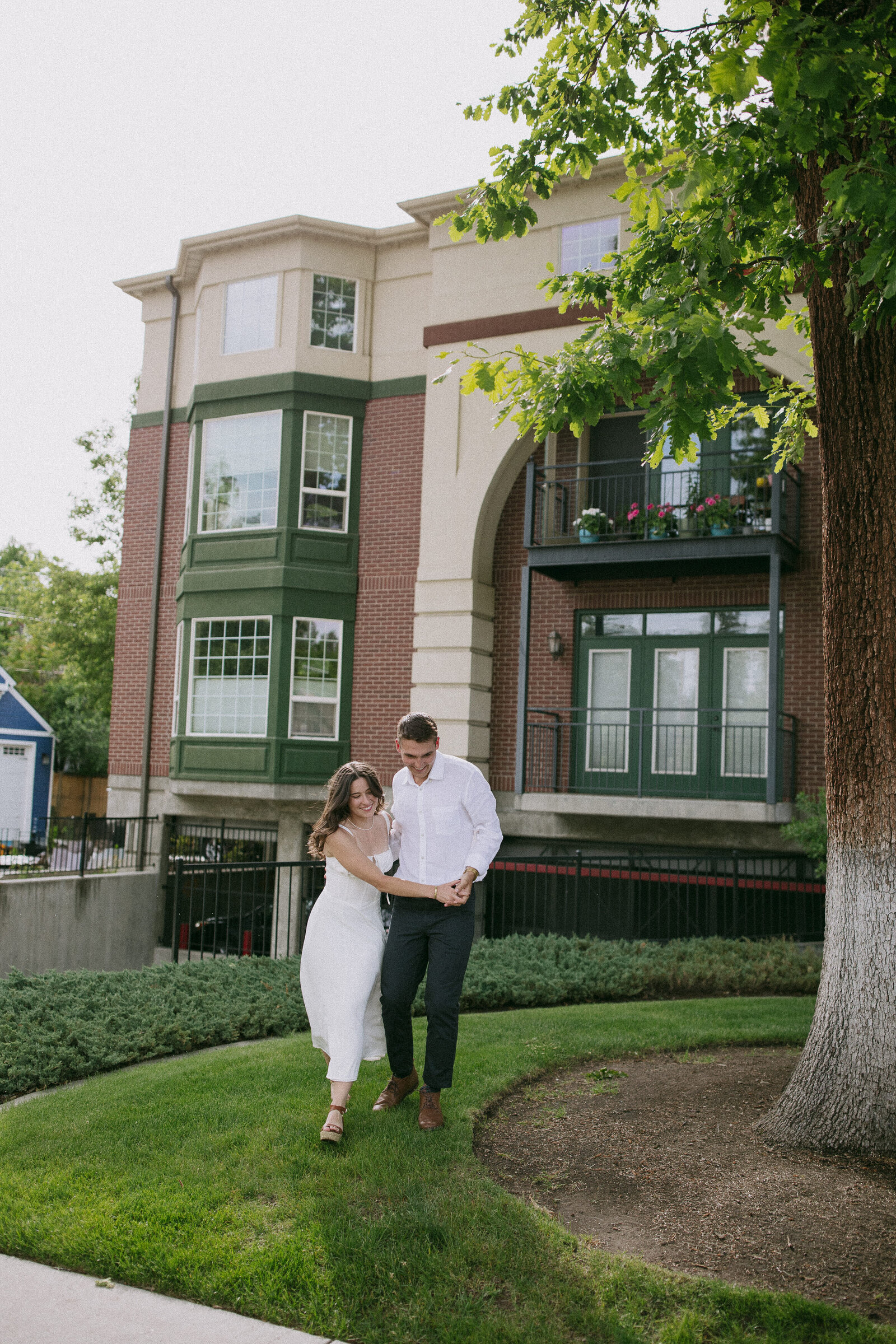 Playful couple running around tree in downtown Coeur d'Alene during candid elopement session
