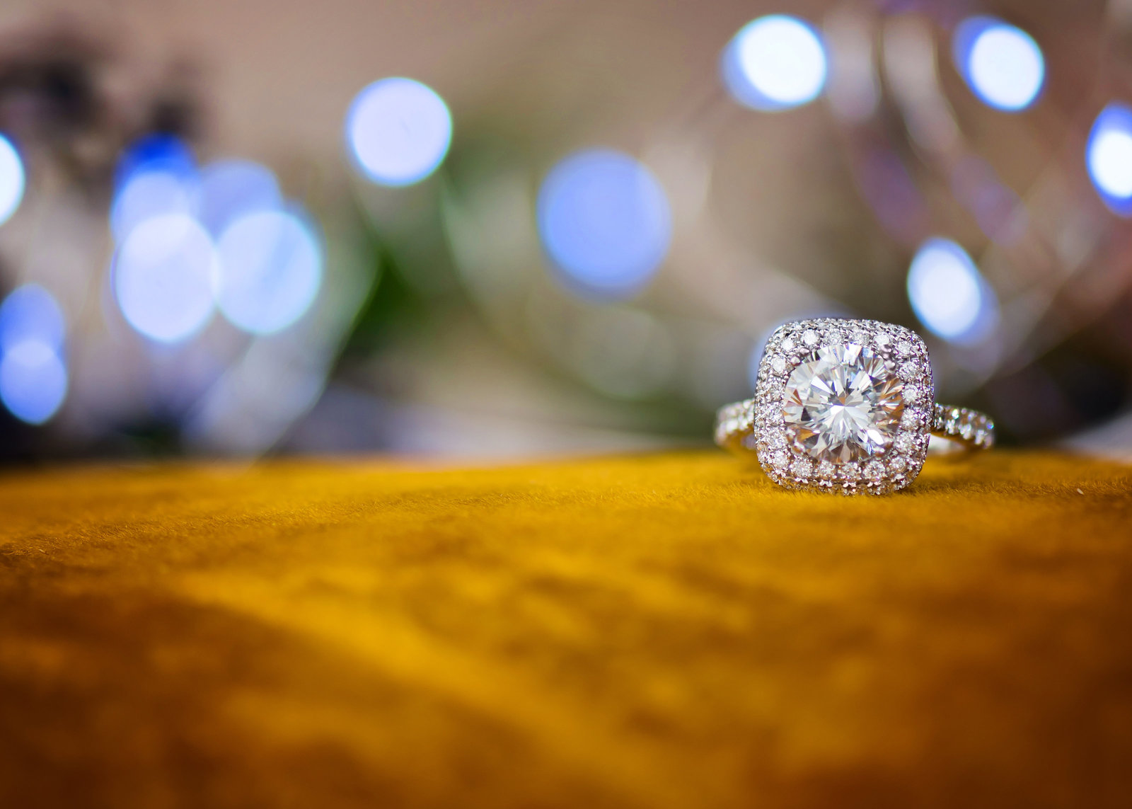 A luxurious five carat, princess cut diamond laying on a ochre velvet cushion.
