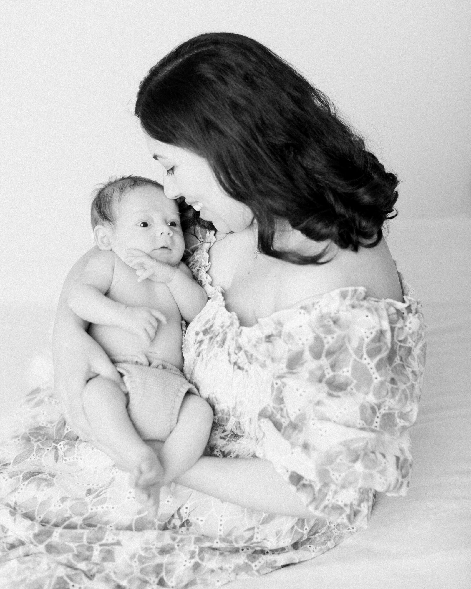 New mom in floral off the shoulder gown cradles her baby and smiles softly at him by NH newborn photographer Fieldstone Studio.